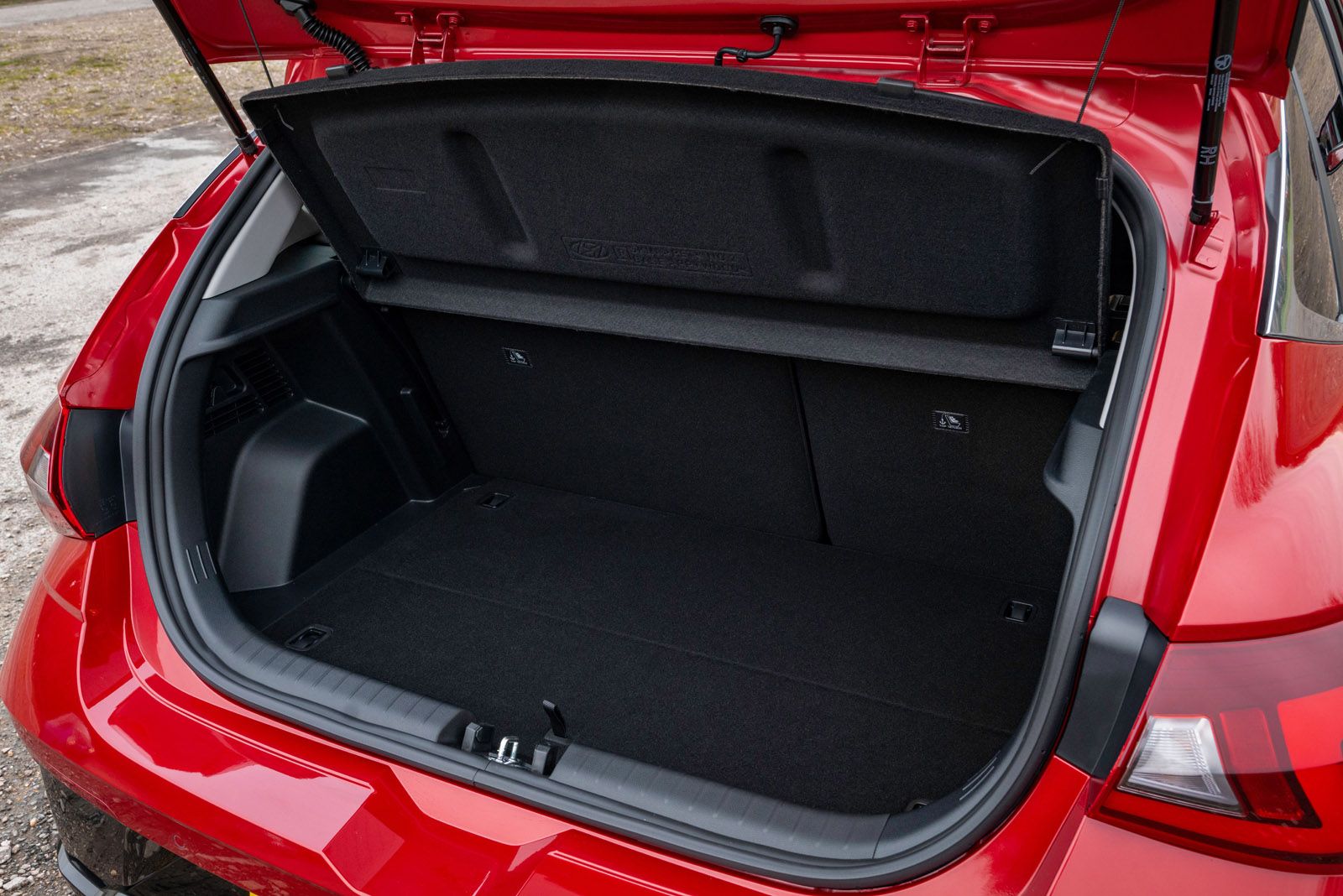 Open trunk of a red car showing a spacious, empty cargo area with a black interior. Trunk cover is raised, and the car is parked outdoors.