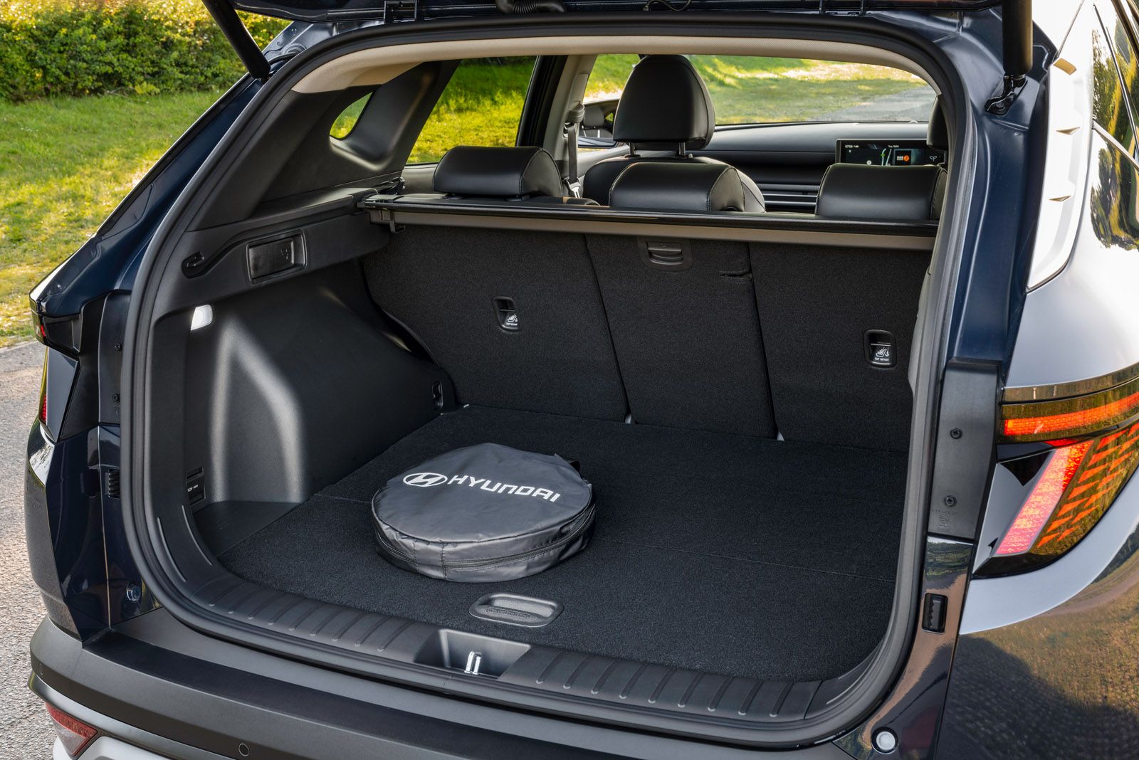 Open trunk of a Hyundai SUV with a folded cargo cover and a Hyundai-branded tire cover inside, parked on a sunny day.