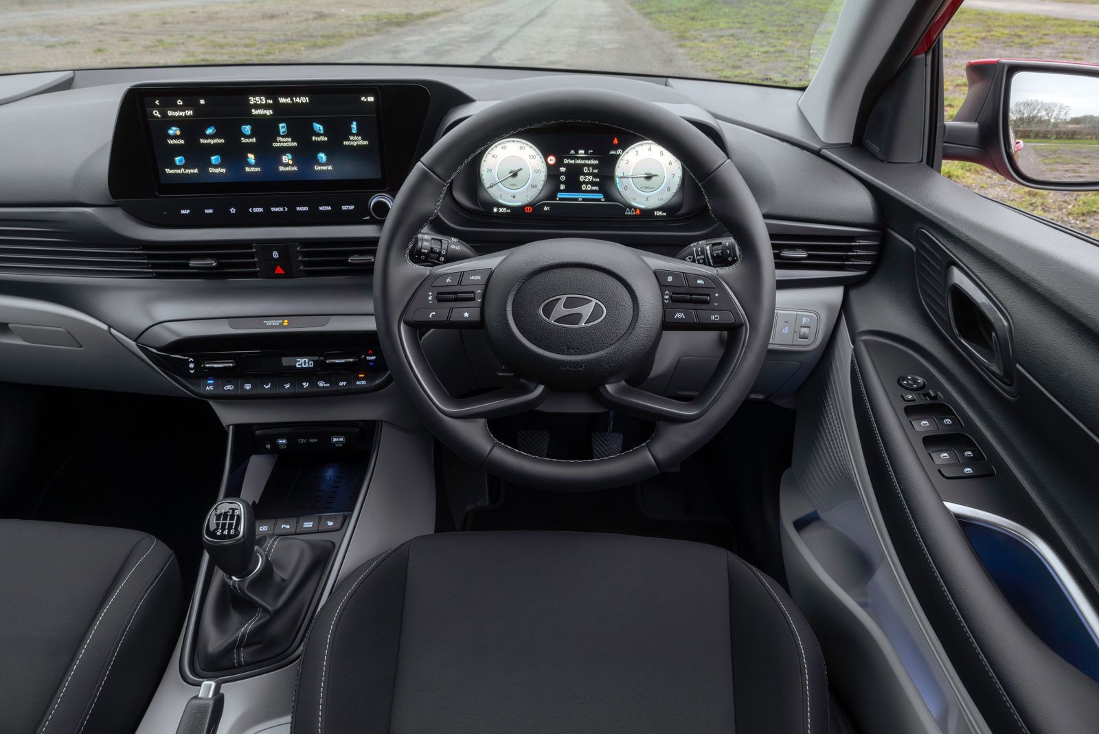 Car interior featuring a steering wheel with control buttons, dual digital displays, manual gear shift, and modern dashboard design.