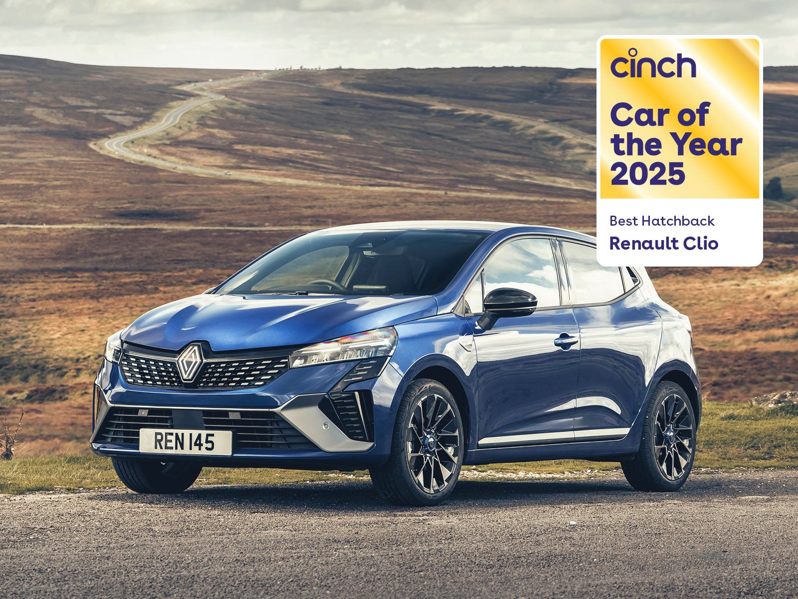 A blue Renault Clio parked on a rural road, awarded "Car of the Year 2025" by Cinch for Best Hatchback, with scenic hills in the background.