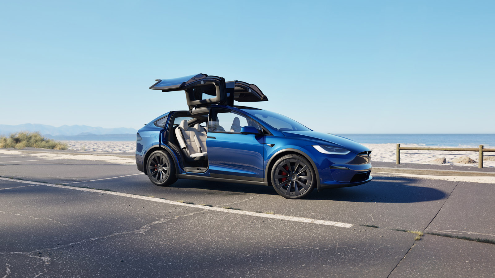 A blue car with falcon-wing doors open, parked on a coastal road with a clear sky and beach in the background.