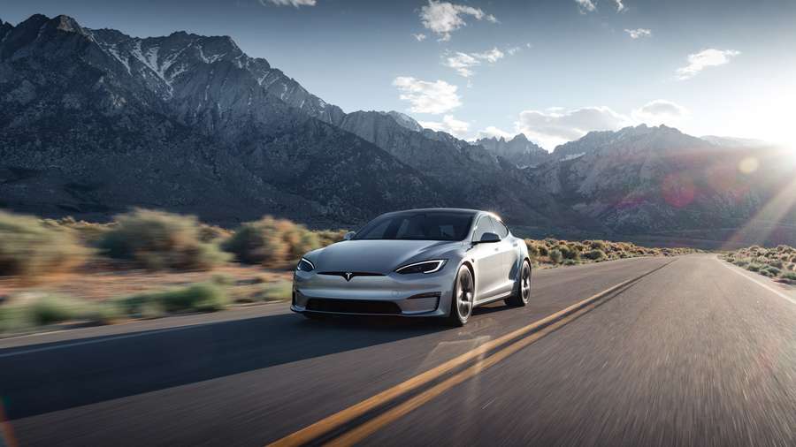 a silver tesla model s driving on a road surrounded by mountains
