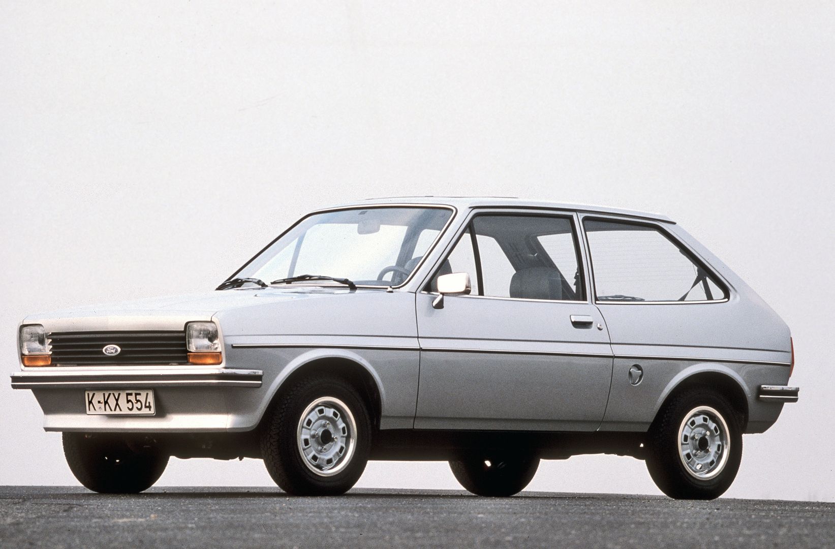 A vintage silver hatchback car with a classic design, parked on a paved surface against a plain background.