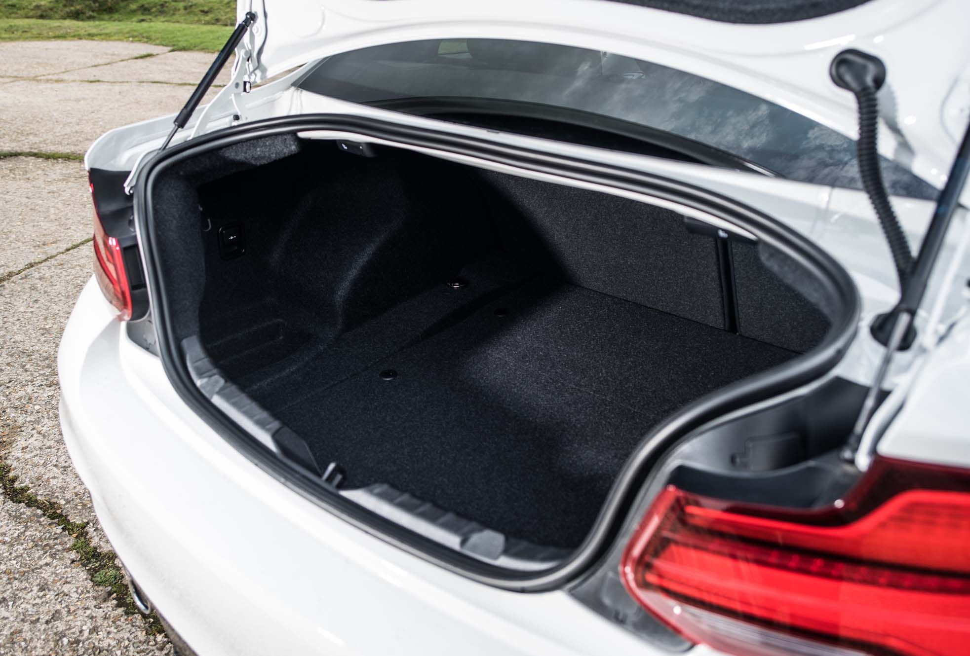 Open boot of a white BMW 2 Series, showcasing a spacious, carpeted cargo area. Tail light partially visible on the right.