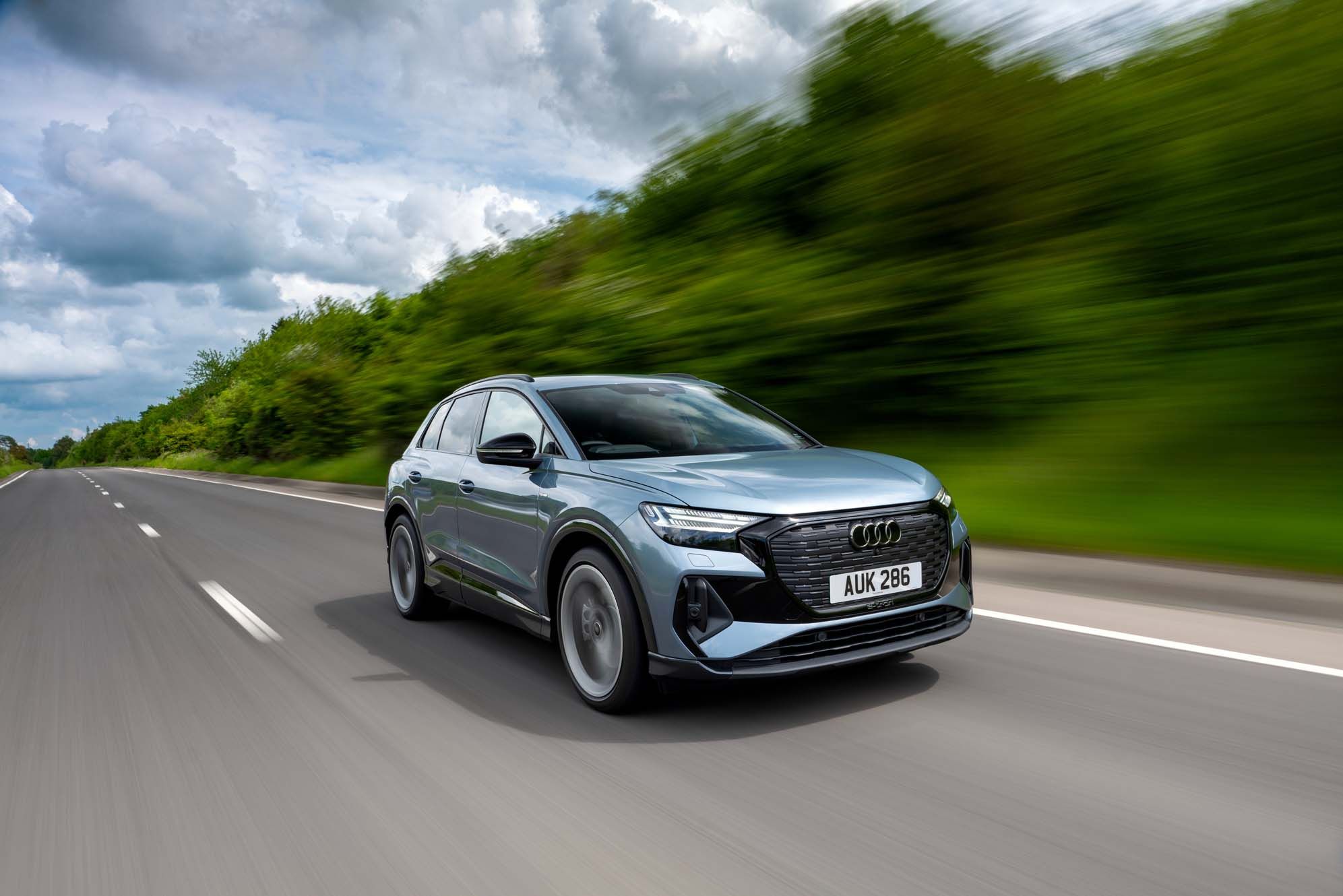 Silver Audi Q4 e-tron driving on a highway with blurred green trees and a cloudy sky in the background.