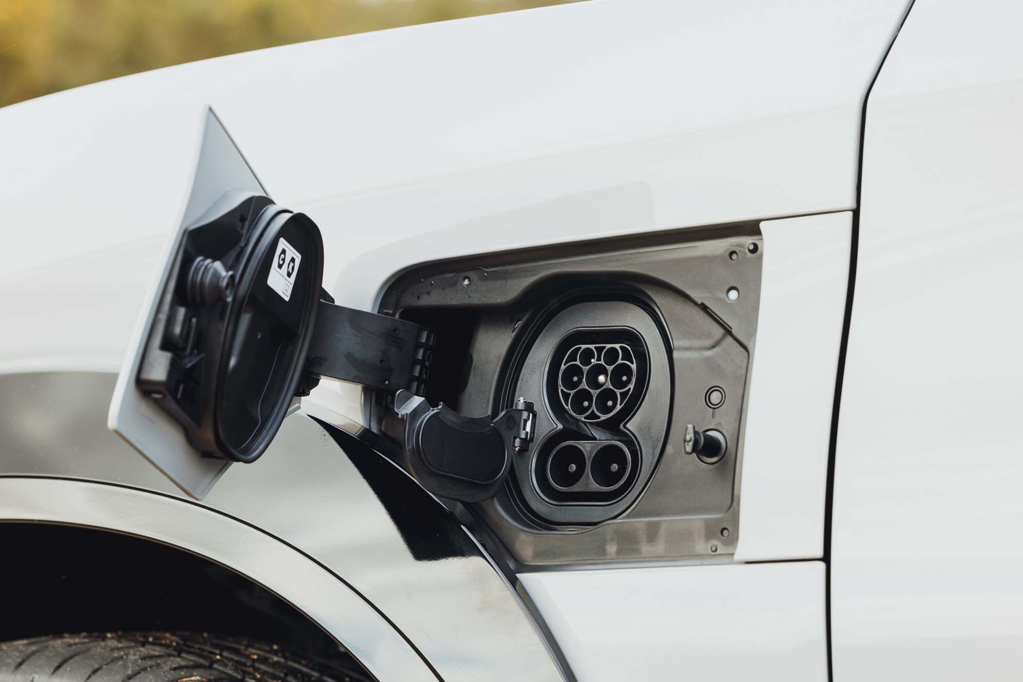 Lexus RZ charging port with its cover open, showing different socket types on a white car.