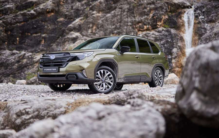 A green Subaru Forester parked on rocky terrain with a waterfall in the background.