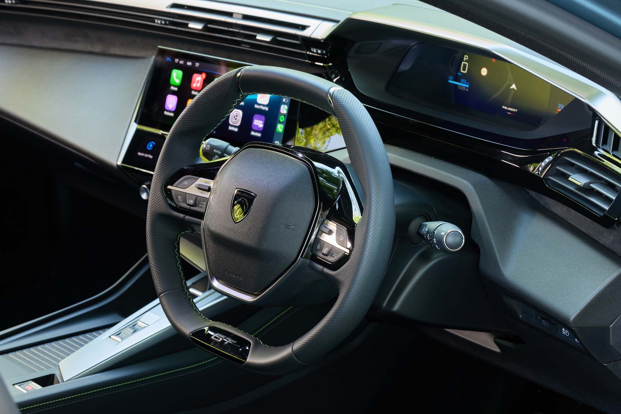 Close-up of a Peugeot E-308 interior featuring a sleek steering wheel with buttons and digital displays on the dashboard and center console.