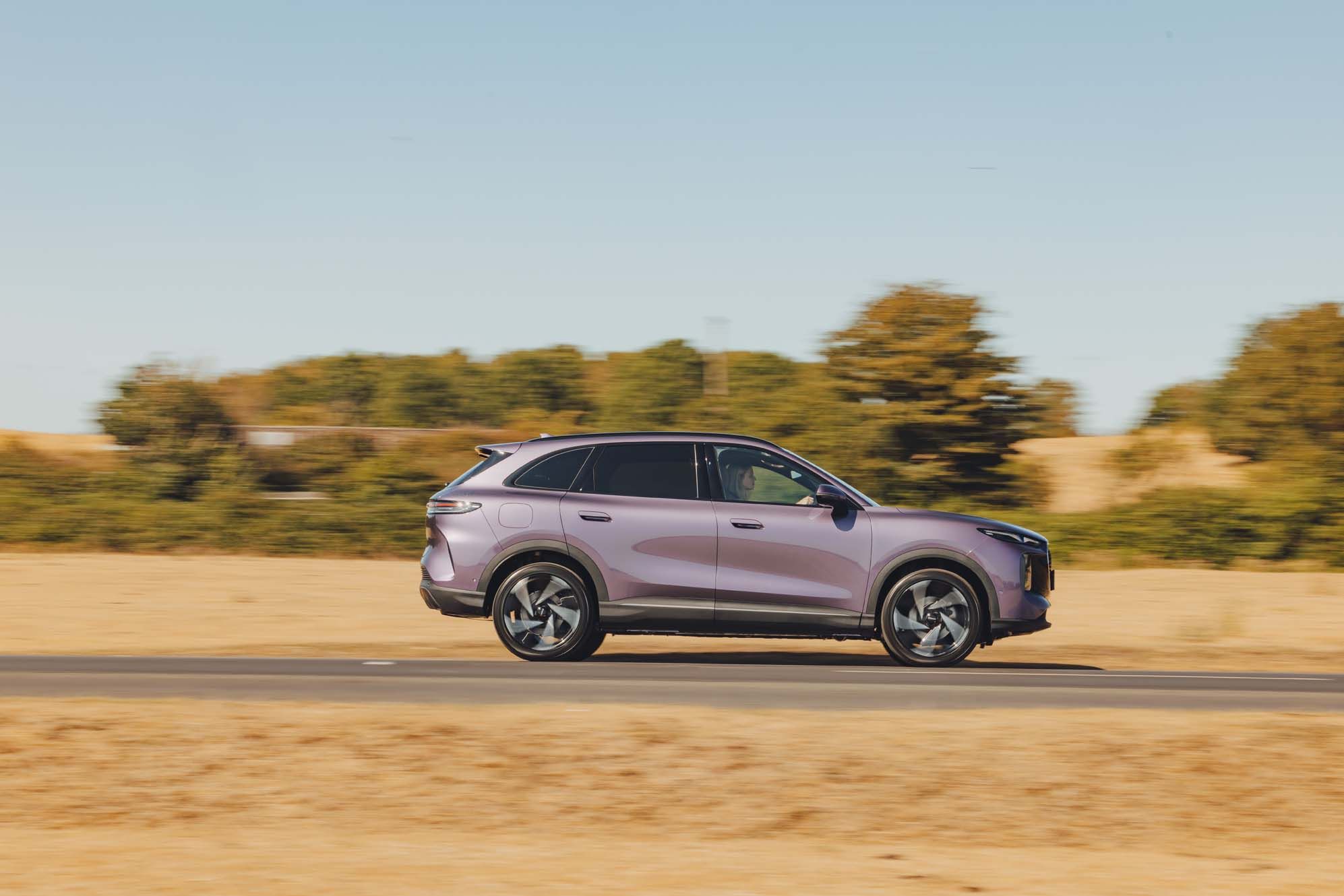 A purple LEPAS L8 driving on a road with blurred motion, surrounded by a grassy landscape and clear blue sky.
