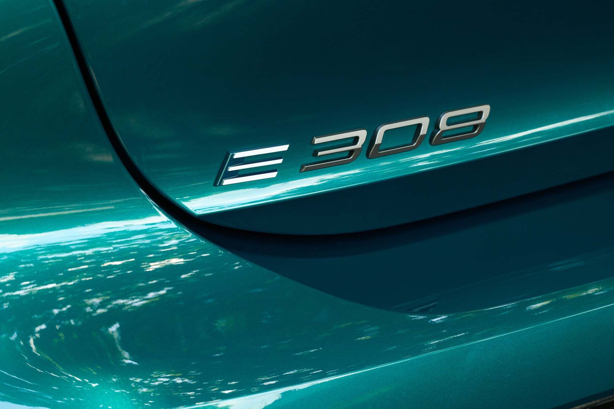 Close-up of a Peugeot E-308 with the "E-308" logo on the side, reflecting sunlight.