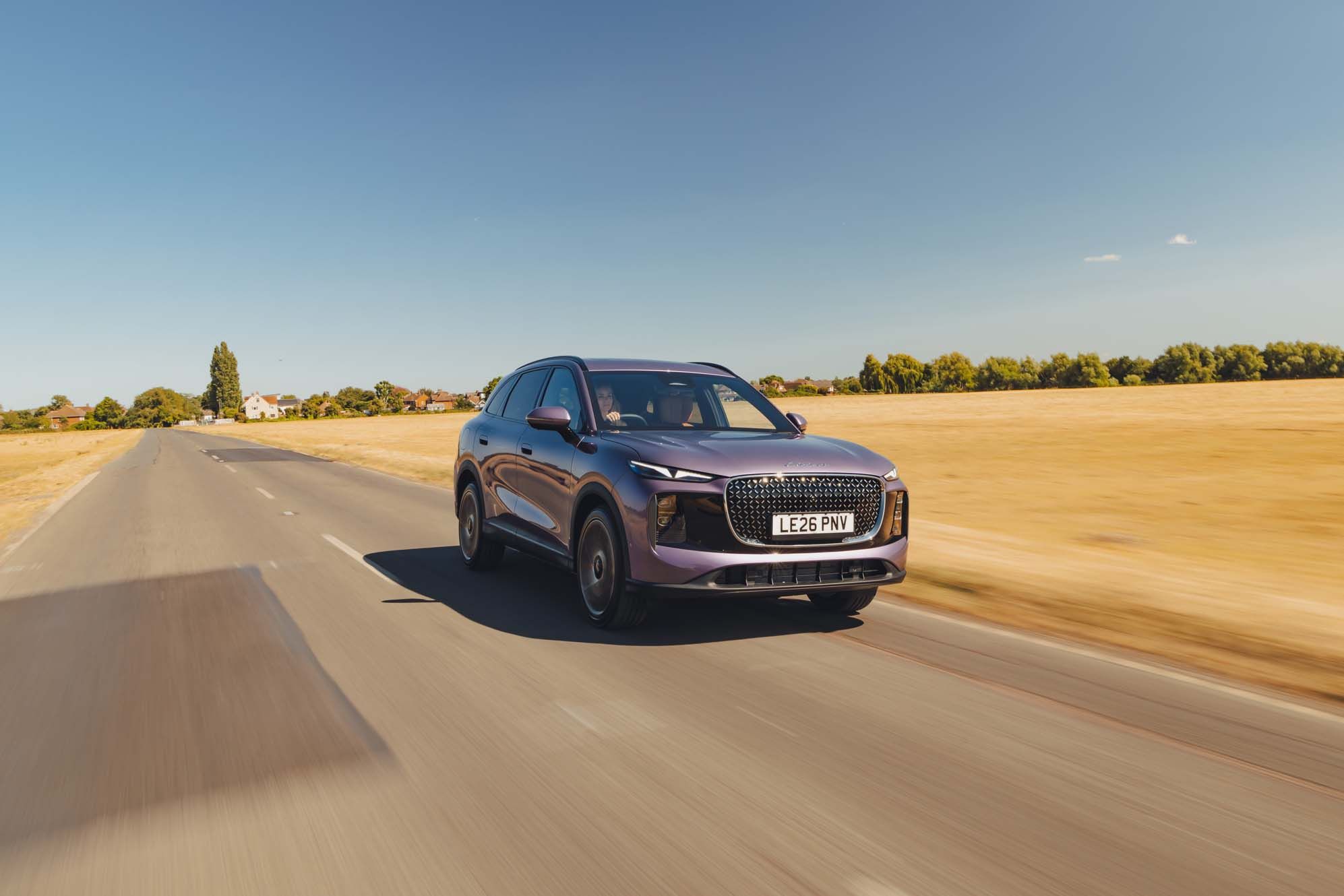 A purple LEPAS L8 drives down a rural road under a clear blue sky, surrounded by golden fields.