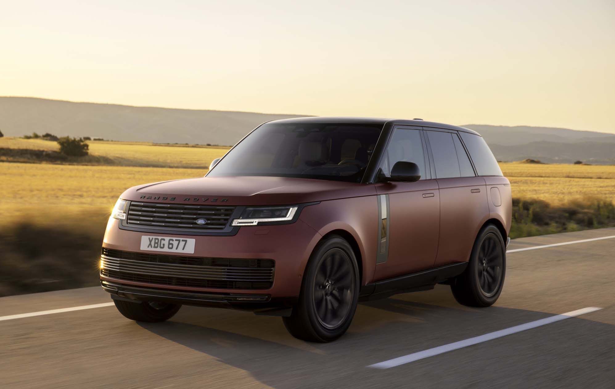 A maroon Range Rover drives on a rural road at sunset, with fields and distant hills in the background.