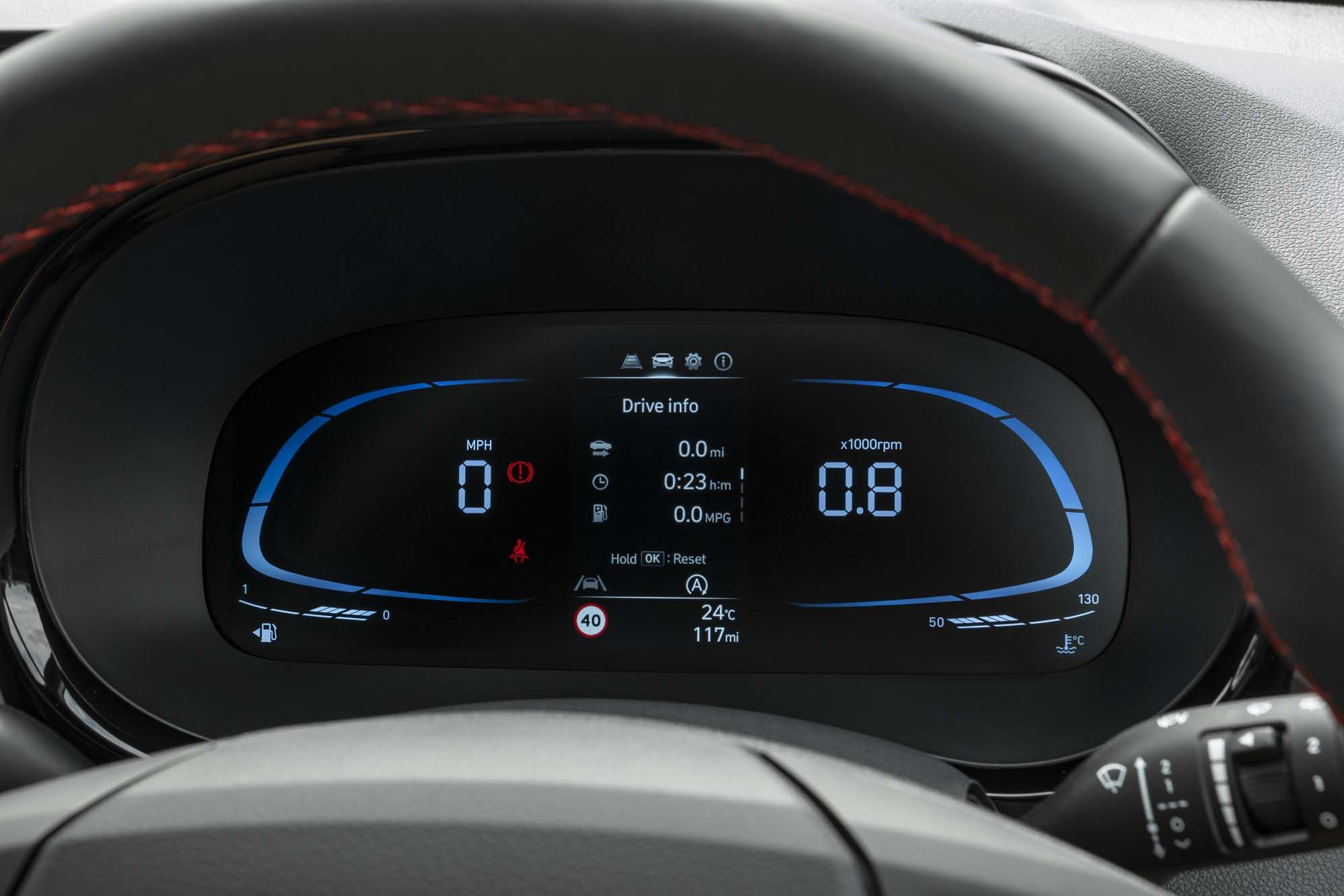 Close-up of a Hyundai i10's digital dashboard displaying speed, RPM, drive info, and temperature in a sleek, modern design with blue accents.