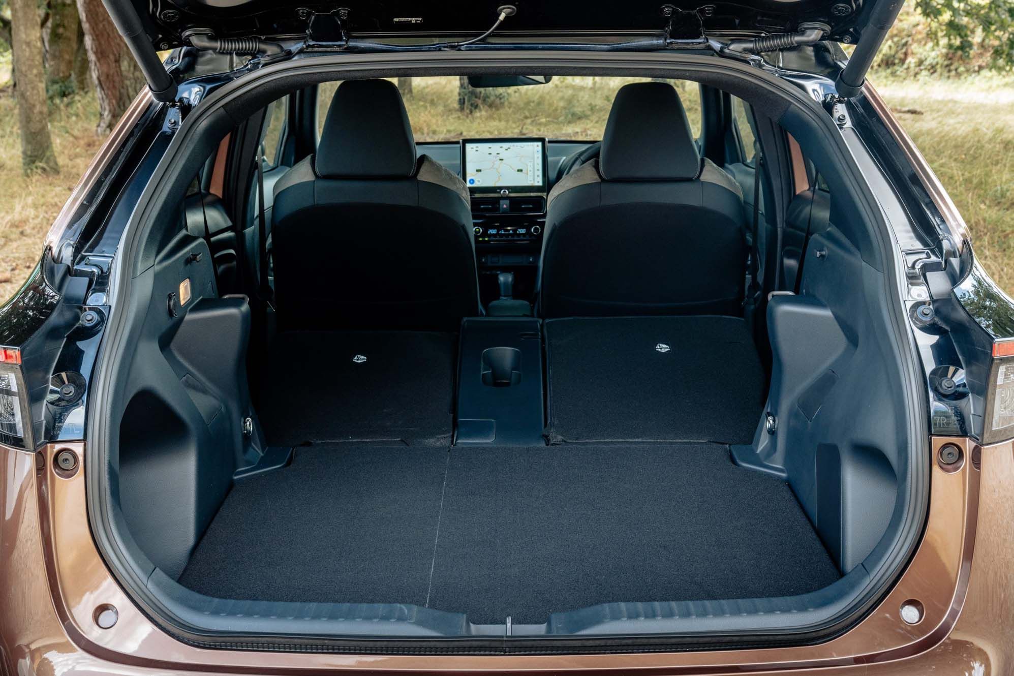 Open boot of a Toyota Yaris Cross with rear seats folded flat, creating spacious cargo area, and a visible navigation screen in the front of the vehicle.