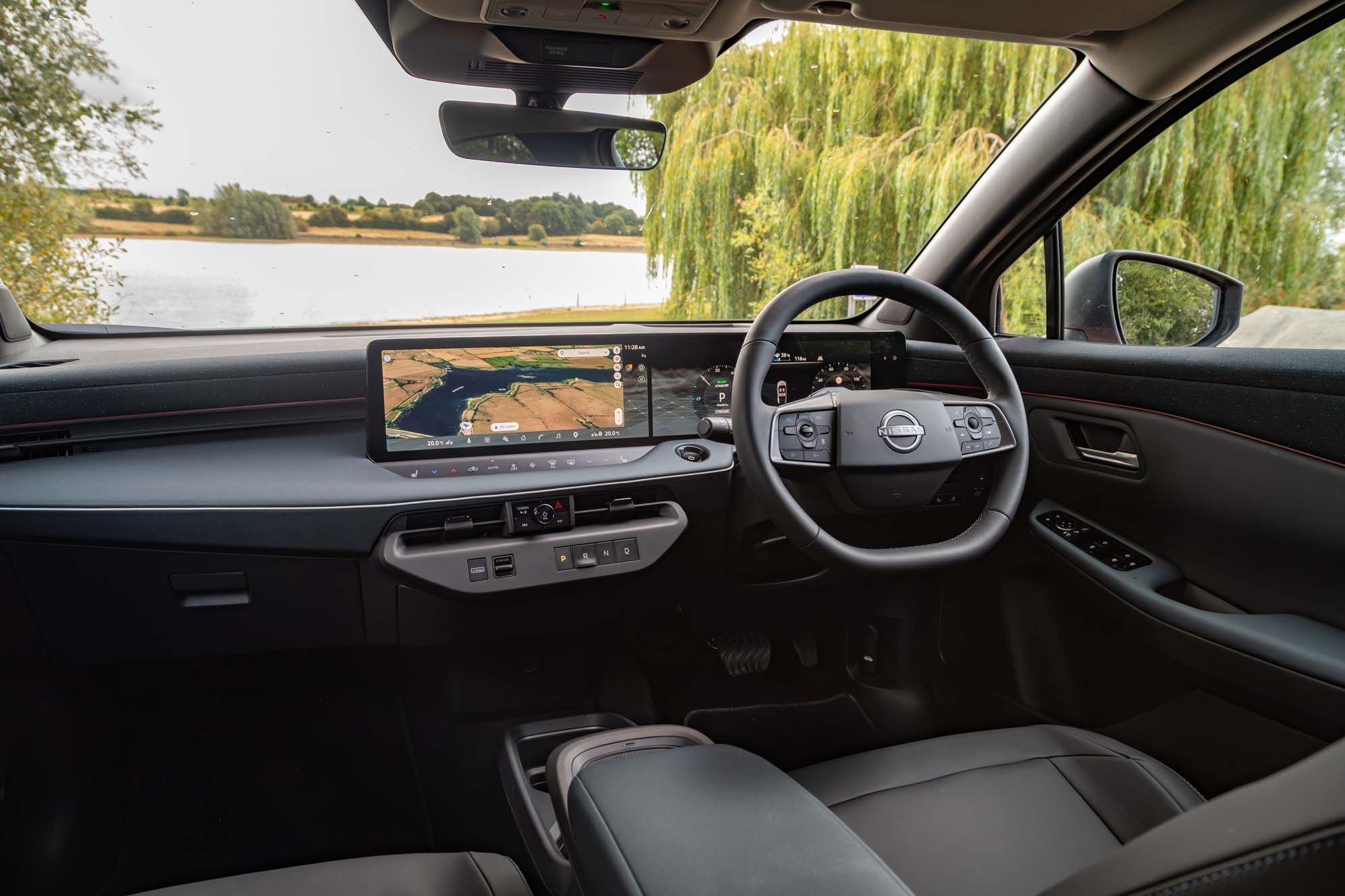 Interior of a Nissan LEAF featuring a modern dashboard with a digital display showing navigation, sleek steering wheel, and a scenic lake view outside.