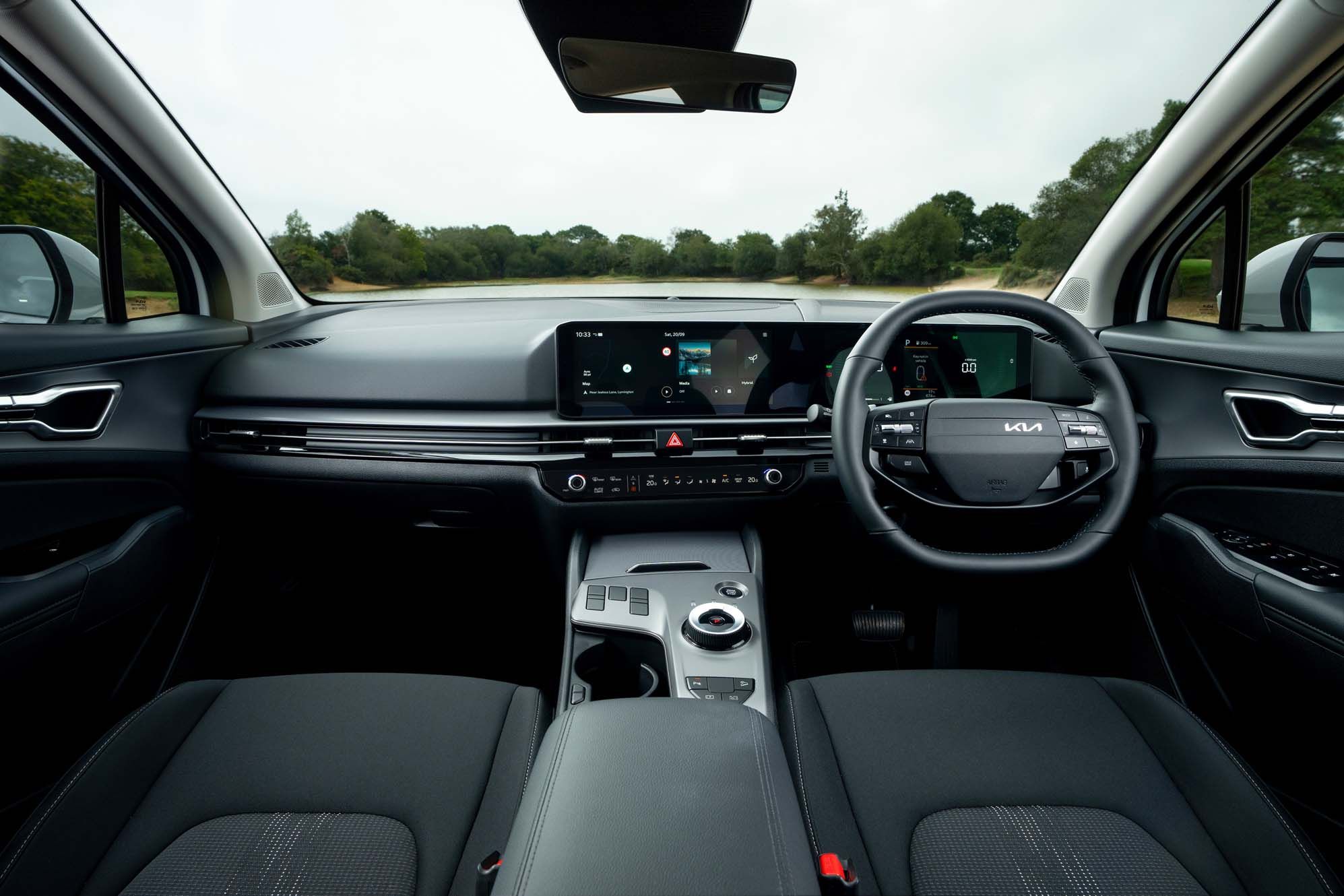 Interior view of a Kia Sportage's dashboard with a digital display, steering wheel with controls, and sleek design elements in a black and grey colour scheme.