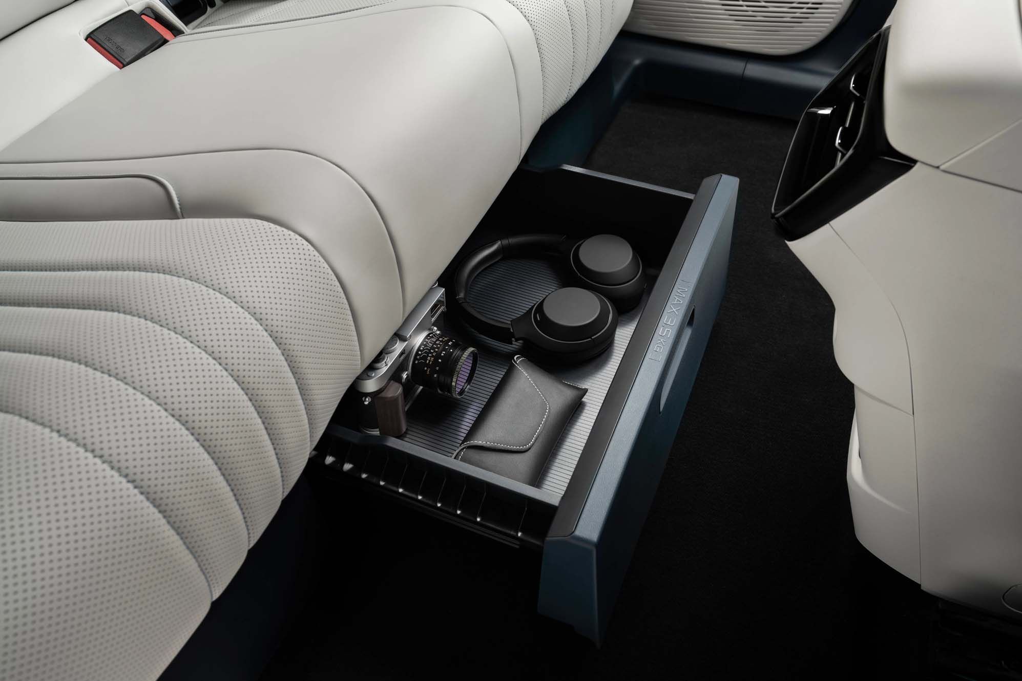 Open car drawer under the back seat of a Geely EX5 with a camera, headphones, and a small pouch inside.
