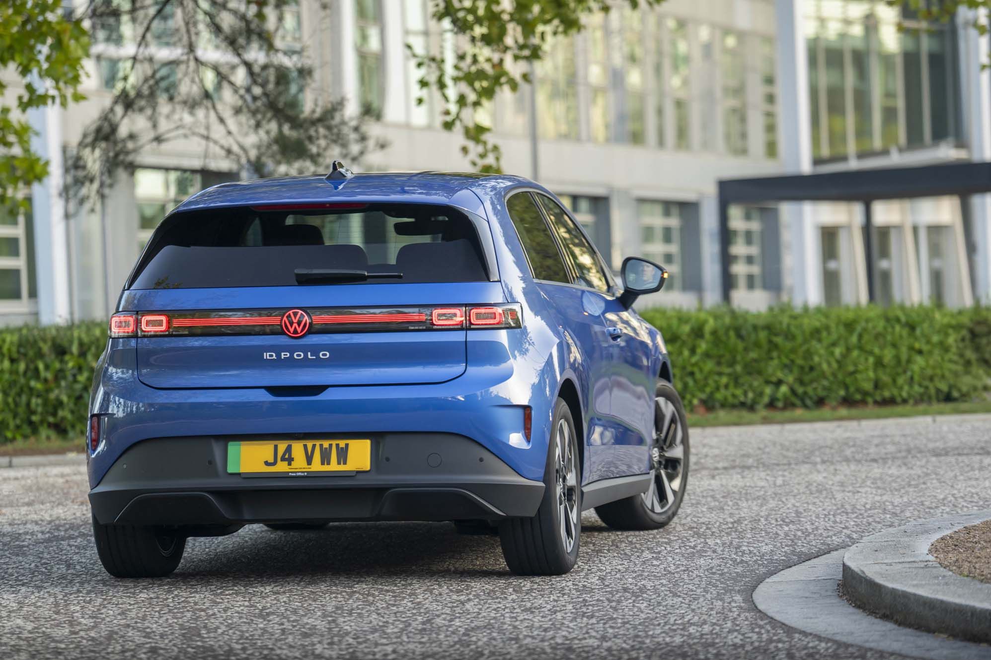 A blue VW ID. Polo is parked on a pavement, near a modern building with large windows.