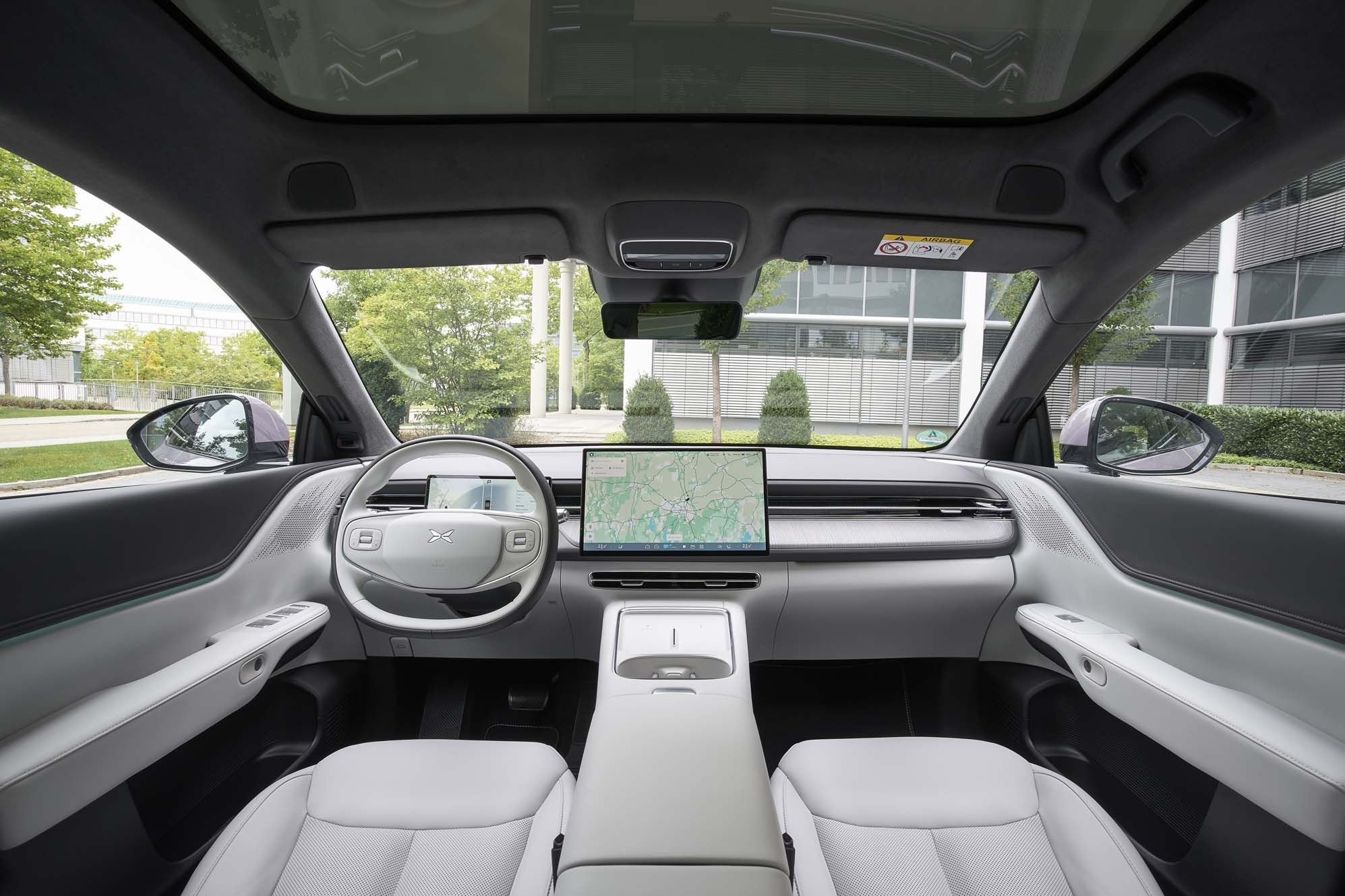 XPENG G6 interior with a panoramic windshield, sleek dashboard, steering wheel, and large central touchscreen displaying a map.