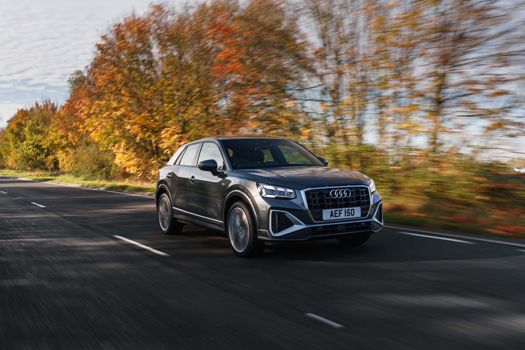 A silver Audi Q2 drives on a road lined with autumn trees, showcasing motion blur and vibrant fall colors.