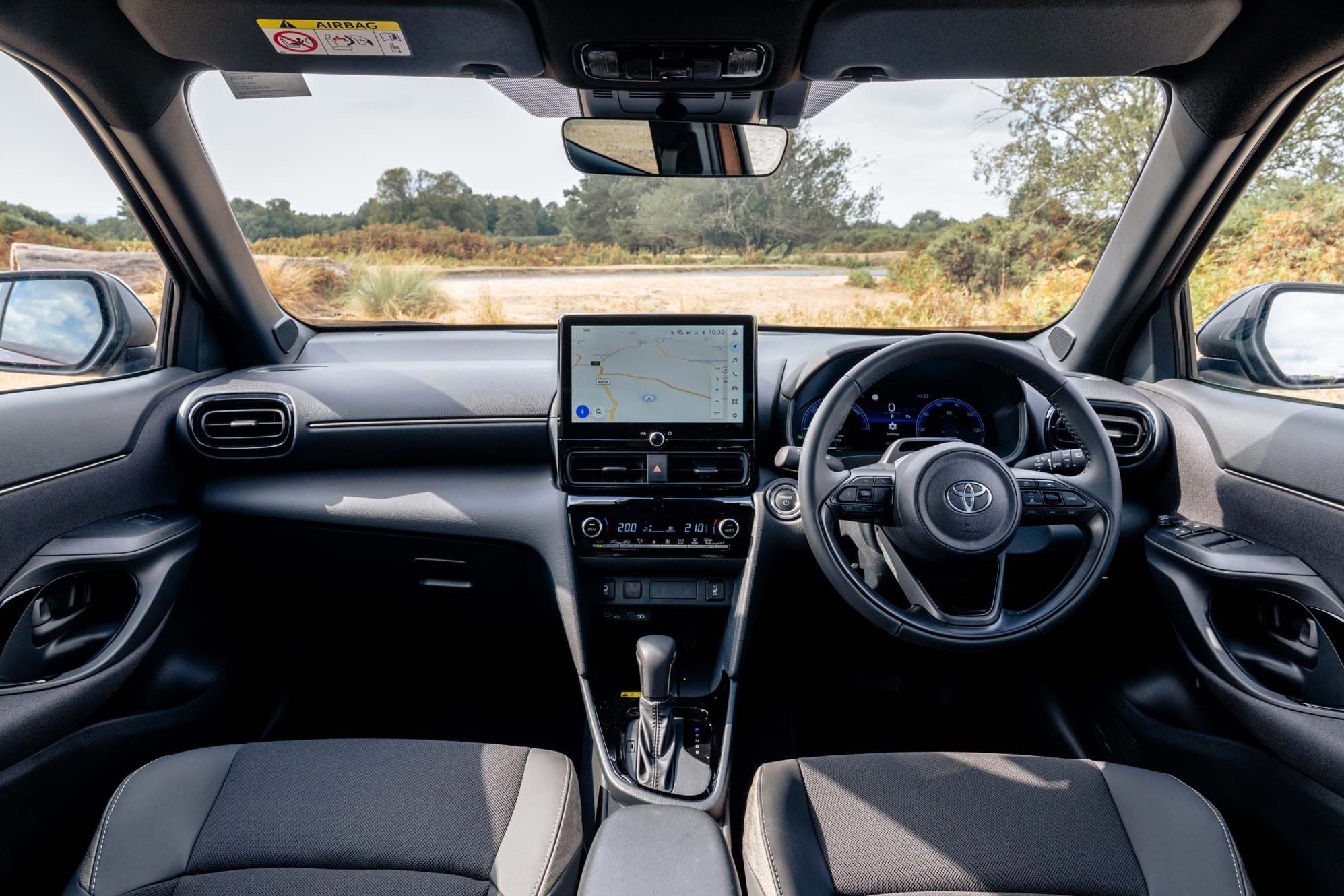 Toyota Yaris Cross interior with a steering wheel, centre console with a GPS screen, and two front seats, looking out to a rural landscape.