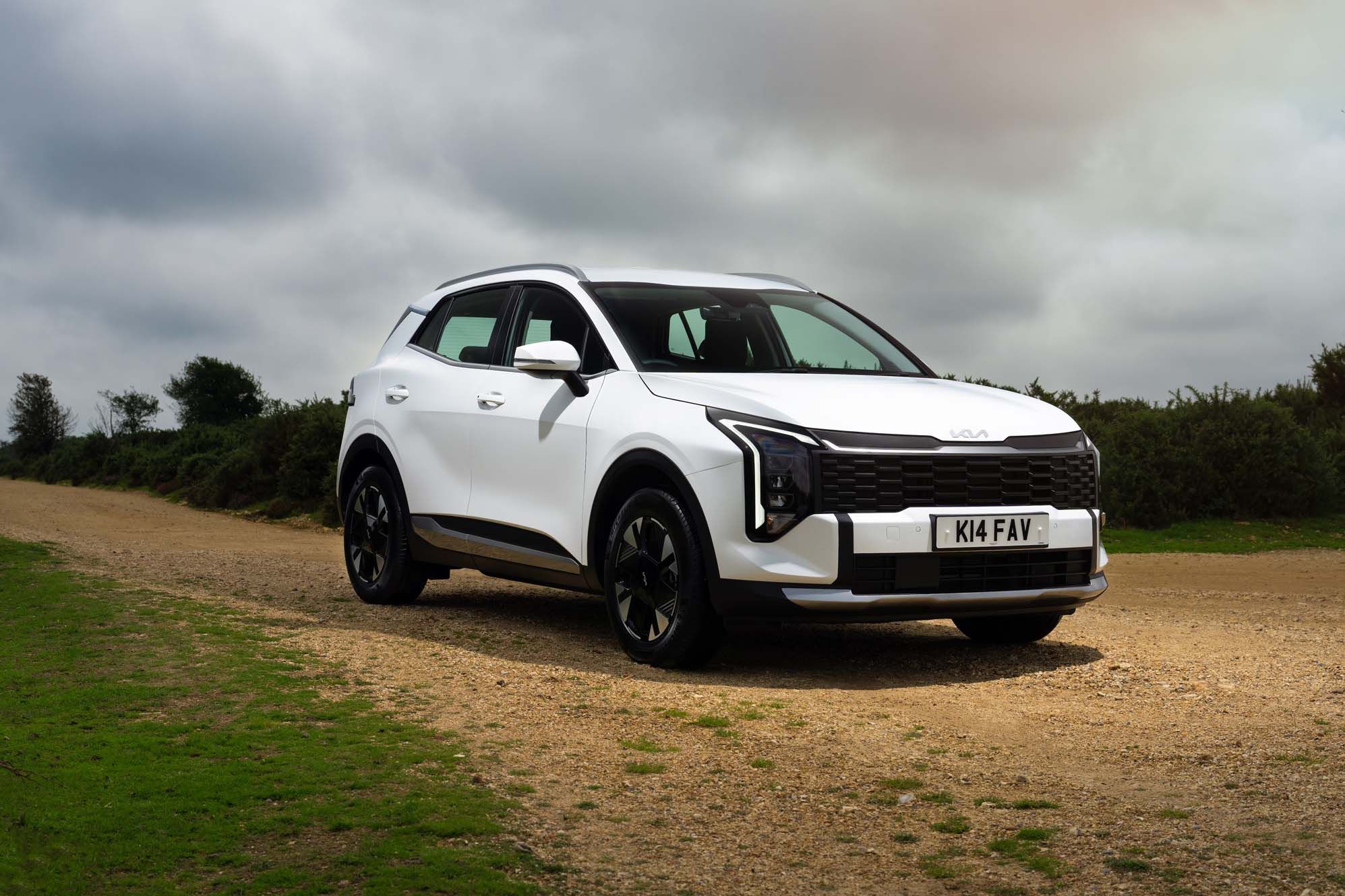 White Kia Sportage parked on a dirt road with cloudy sky; modern design features black trim and sleek lines.