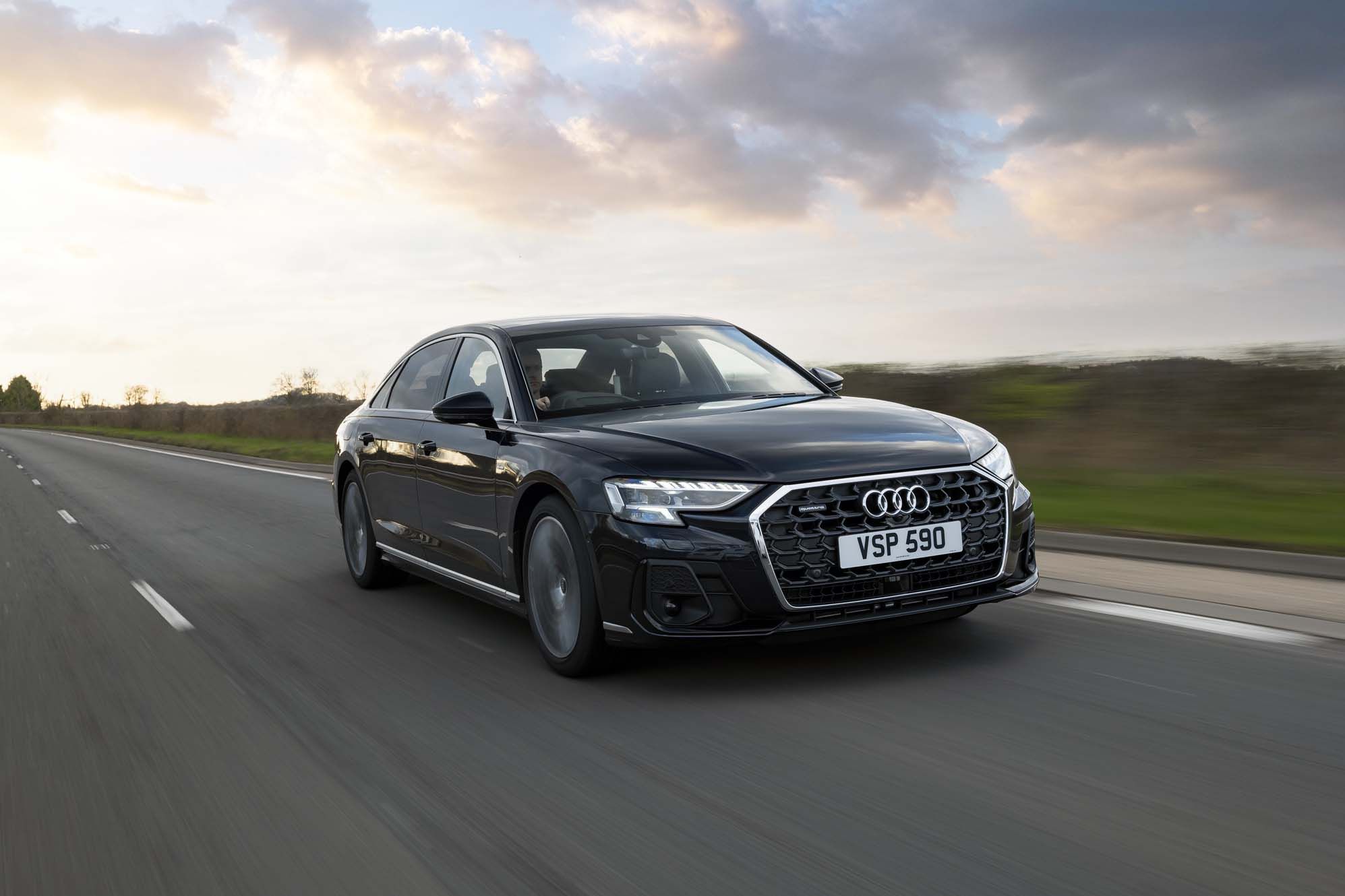 Black Audi A8 driving on an open road at sunset, with blurred motion and a scenic sky in the background.