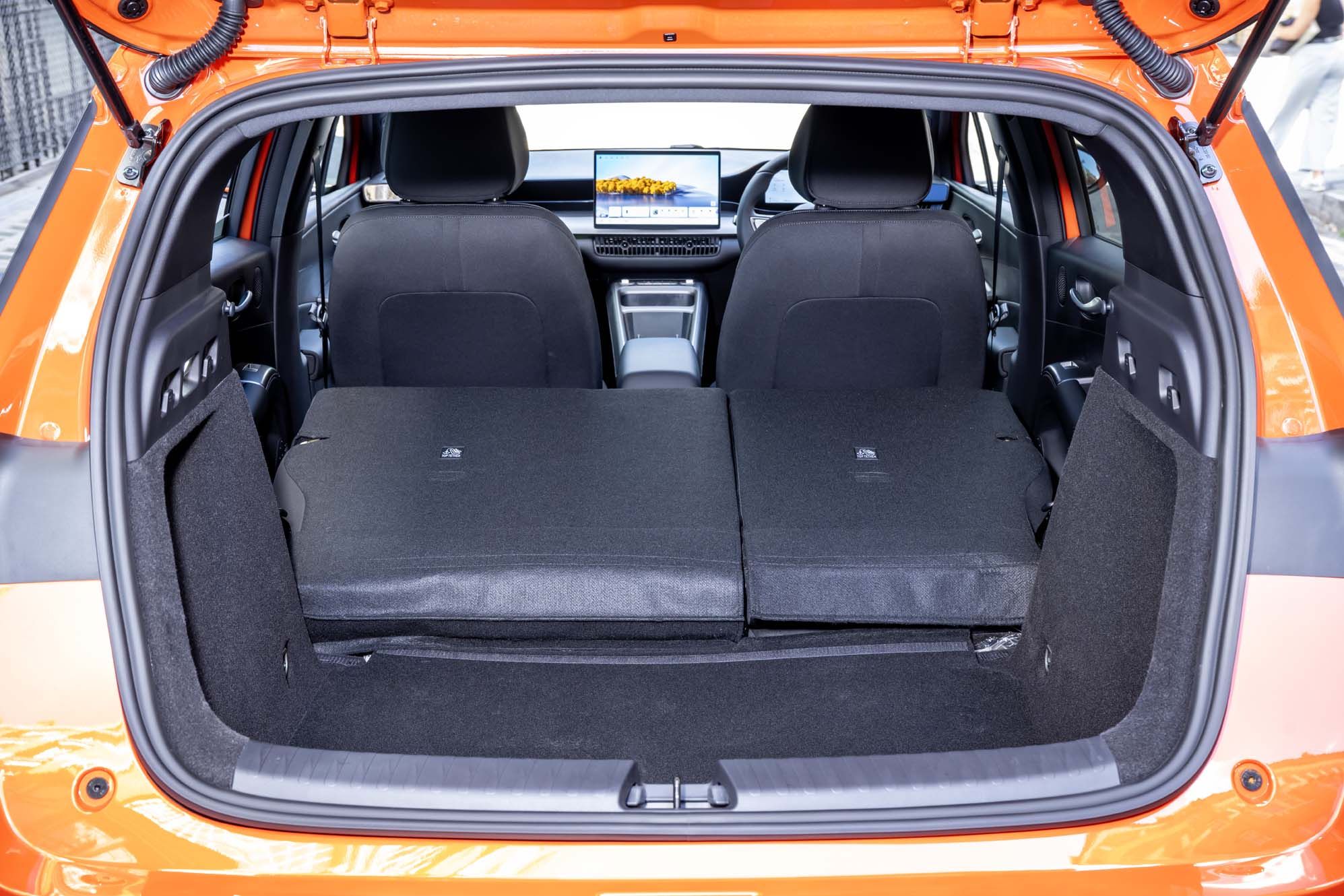Rear view of an orange BYD DOLPHIN G DM-i's open hatchback showing folded back seats and a dashboard screen in the interior.