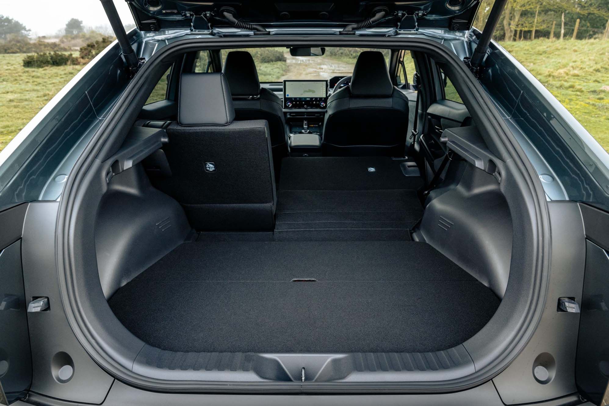 Open boot of a Toyota C-HR+ with rear seats folded down, revealing a spacious cargo area. Outdoors scene in the background.