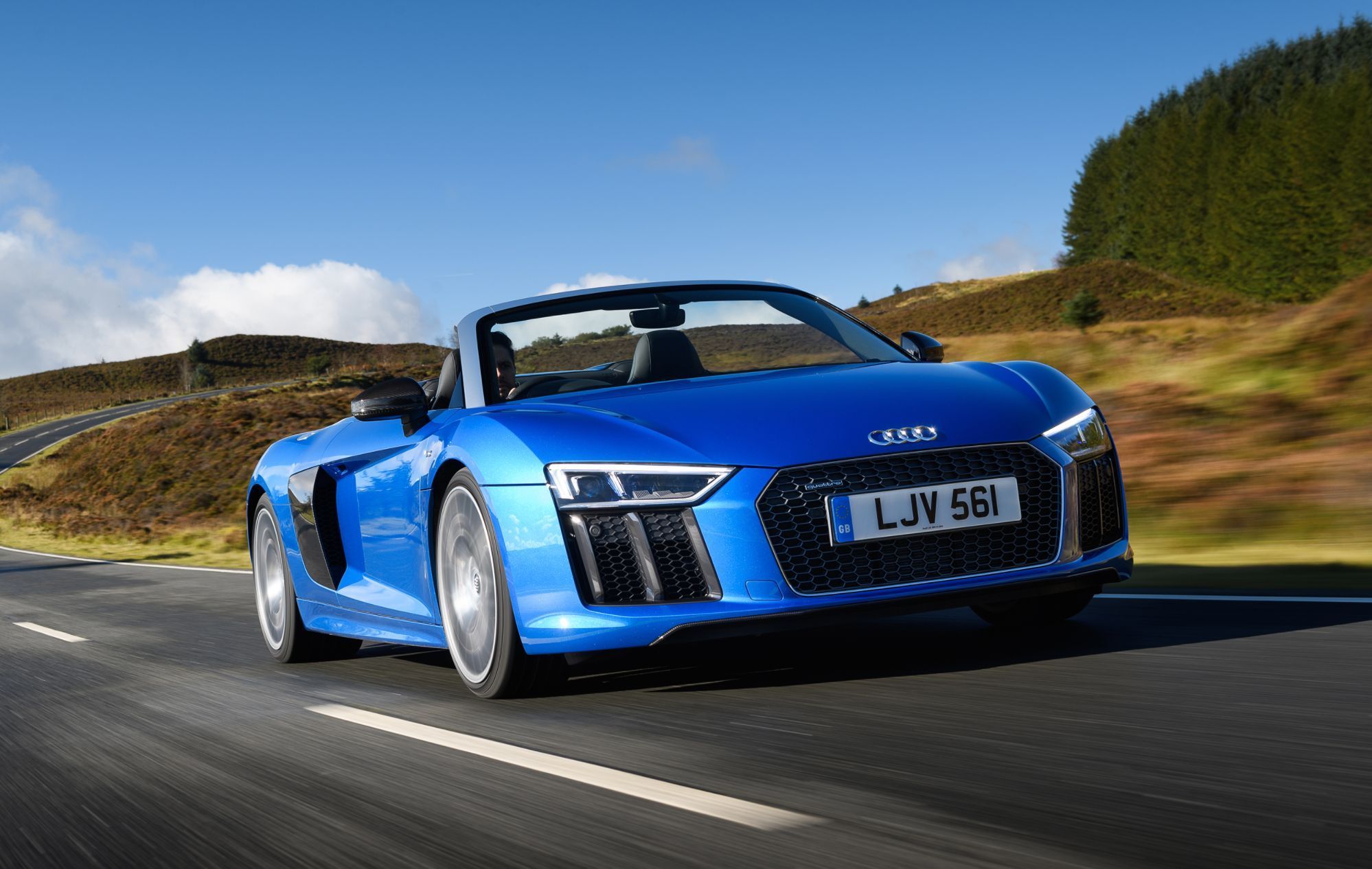 a blue audi r8 v10 plus convertible driving on a uk country road