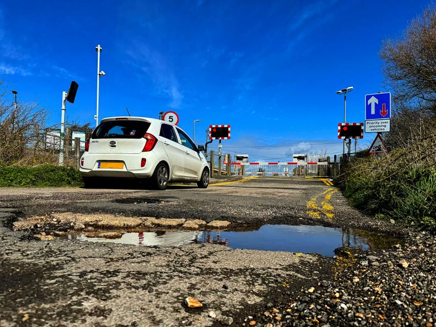 A car parked at a level crossing with a huge pothole