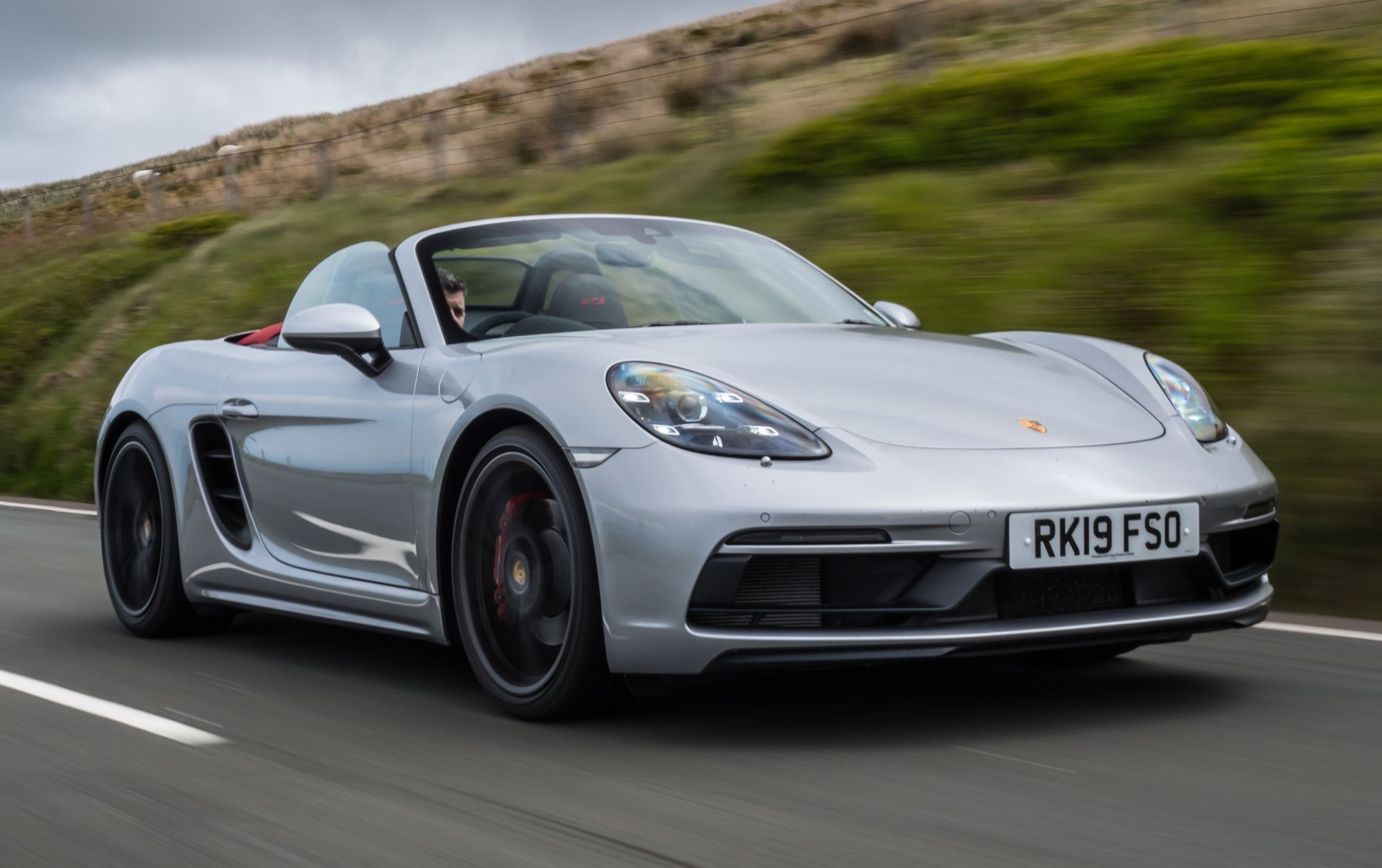 a silver porsche boxster driving on a road