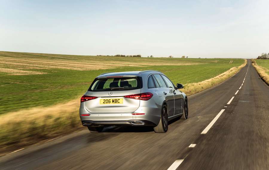 Silver Mercedes C-Class Estate driving on a rural road, flanked by green fields under a clear sky.