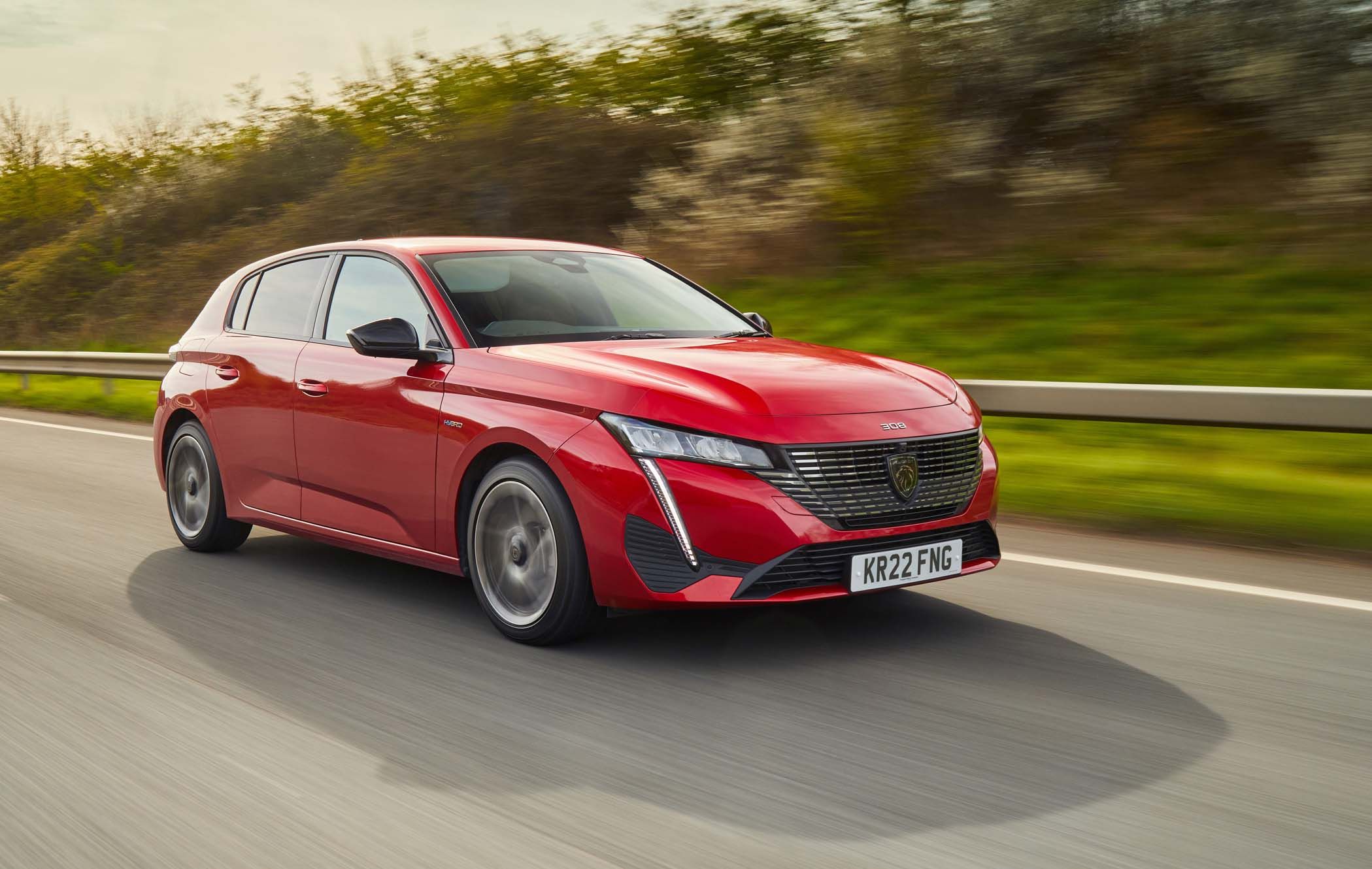 A red Peugeot 308 driving on a road with blurred greenery in the background.