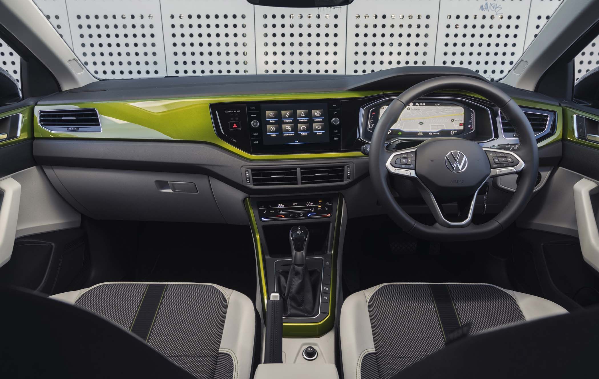 Interior of a VW Taigo showcasing a green-accented dashboard, touchscreen displays, steering wheel, and black and grey seats.