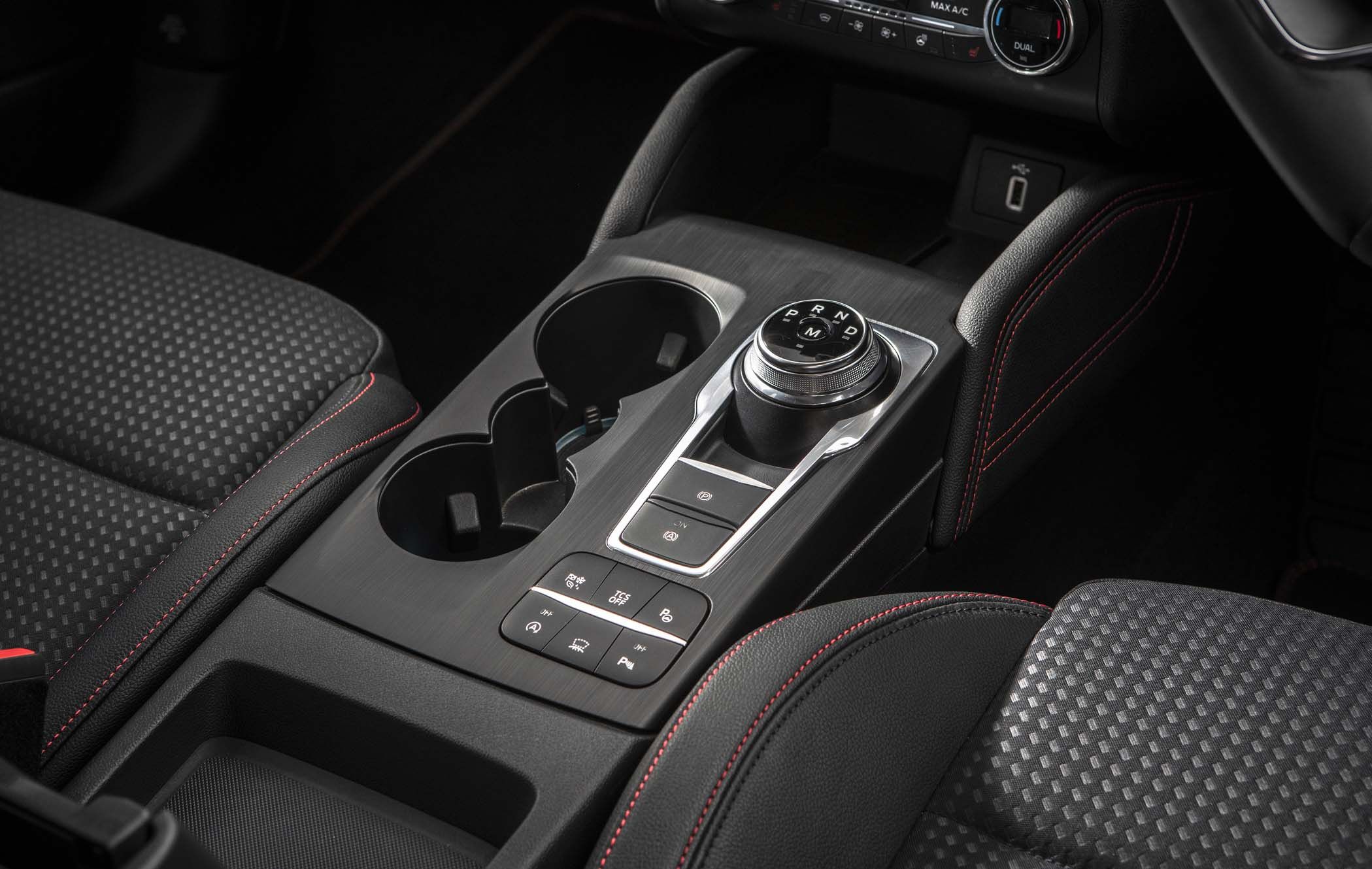 Ford Focus interior showing a centre console with a rotary gear selector, cup holders, and control buttons, featuring black upholstery with red stitching.