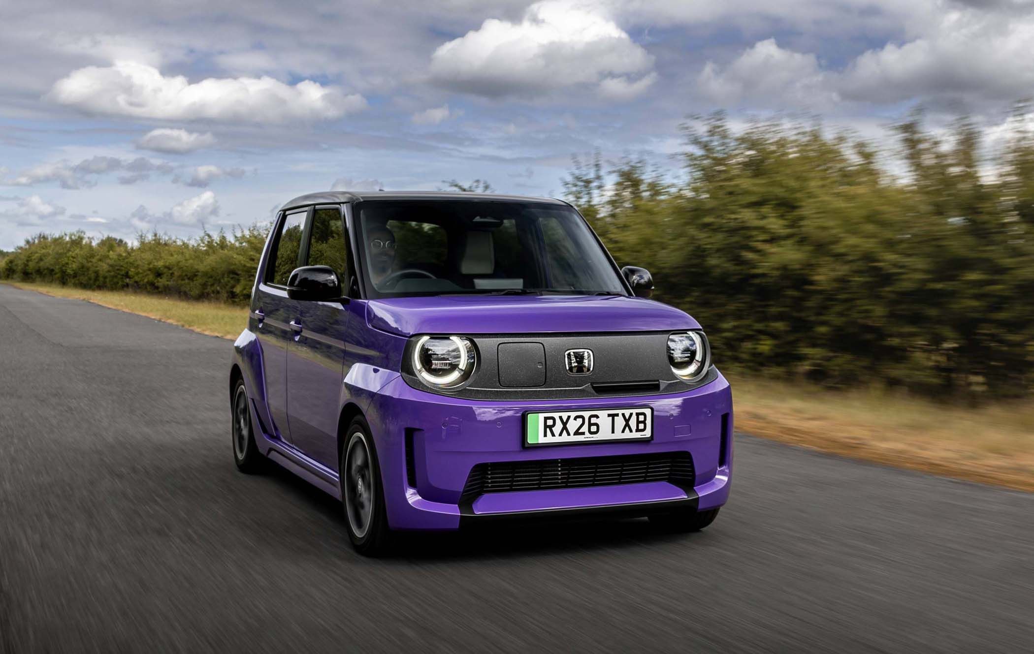 A purple Honda Super-N driving on a rural road with greenery on the side under a cloudy sky.
