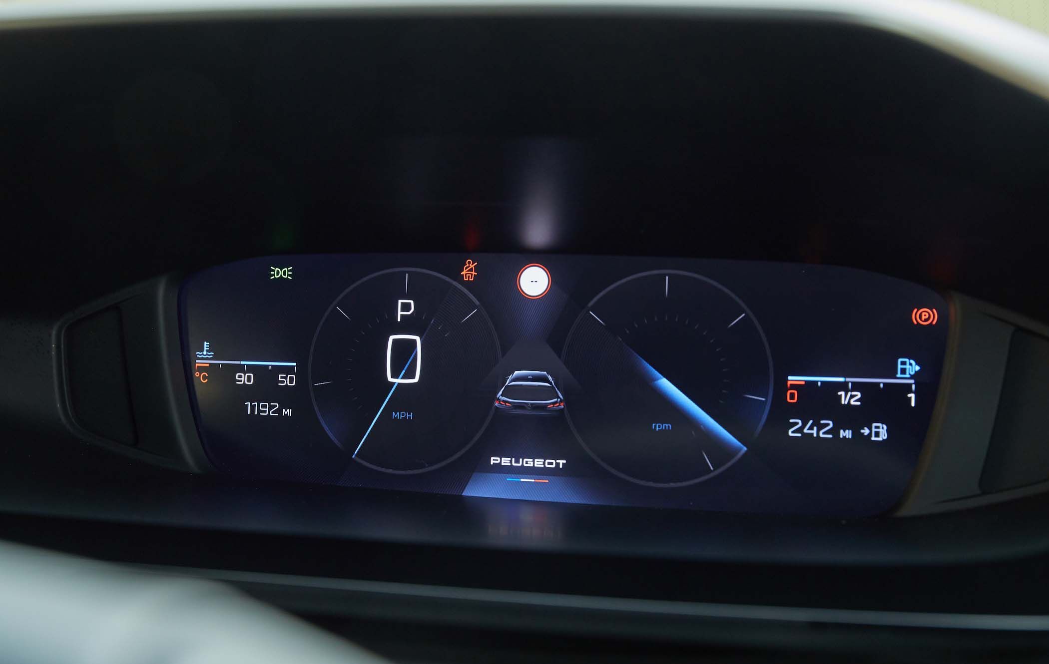 Close-up of a digital car dashboard displaying speed, fuel, temperature, and other indicators, with a central image of a car.
