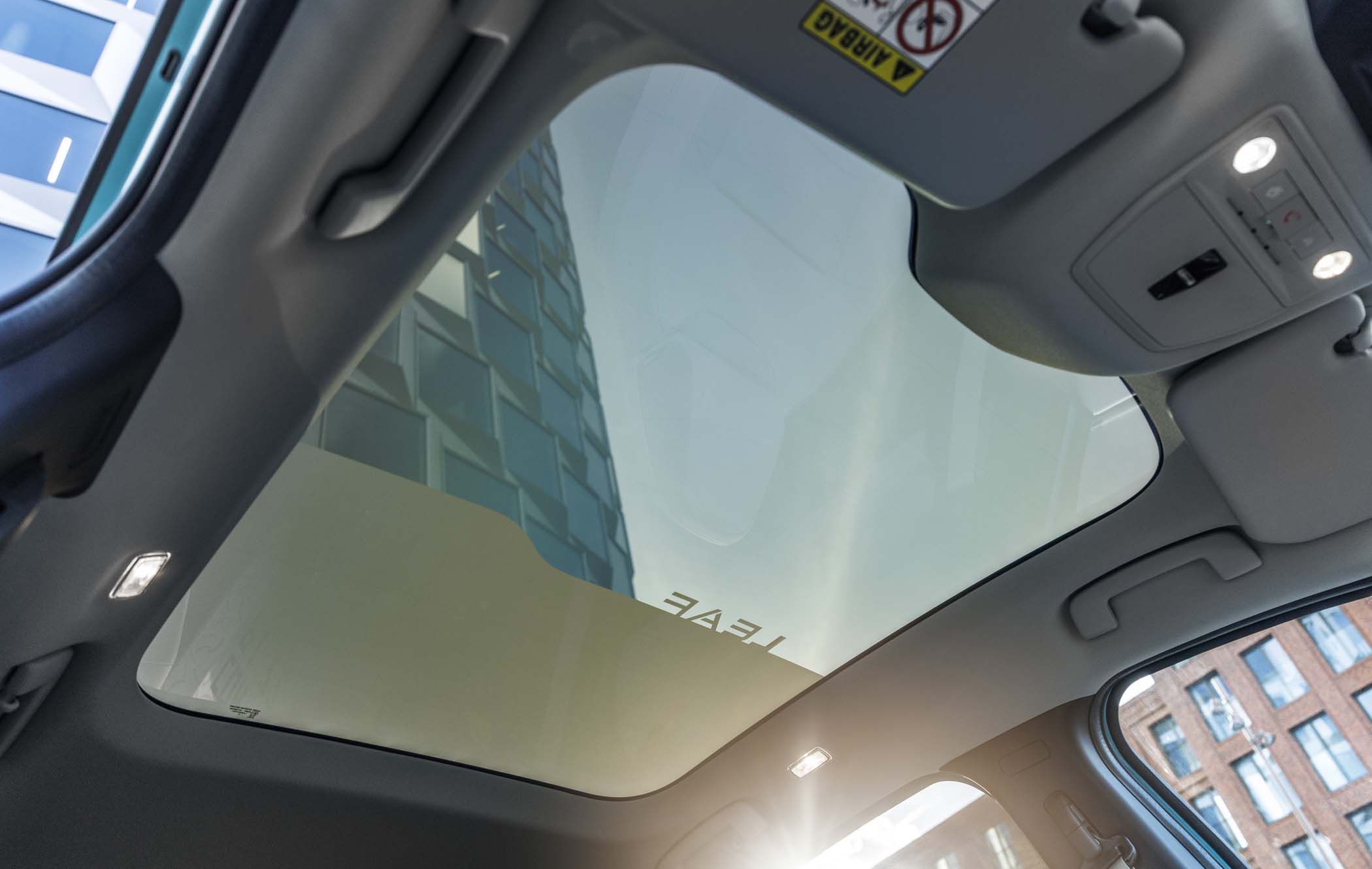 View through a Nissan LEAF panoramic car sunroof showing a modern building under a clear blue sky, interior lights on in the car.