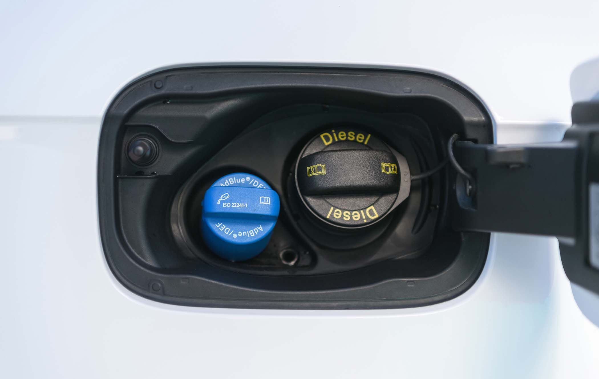 Close-up of Audi Q5's fuel compartment showing a blue AdBlue cap and a black Diesel cap with yellow text.