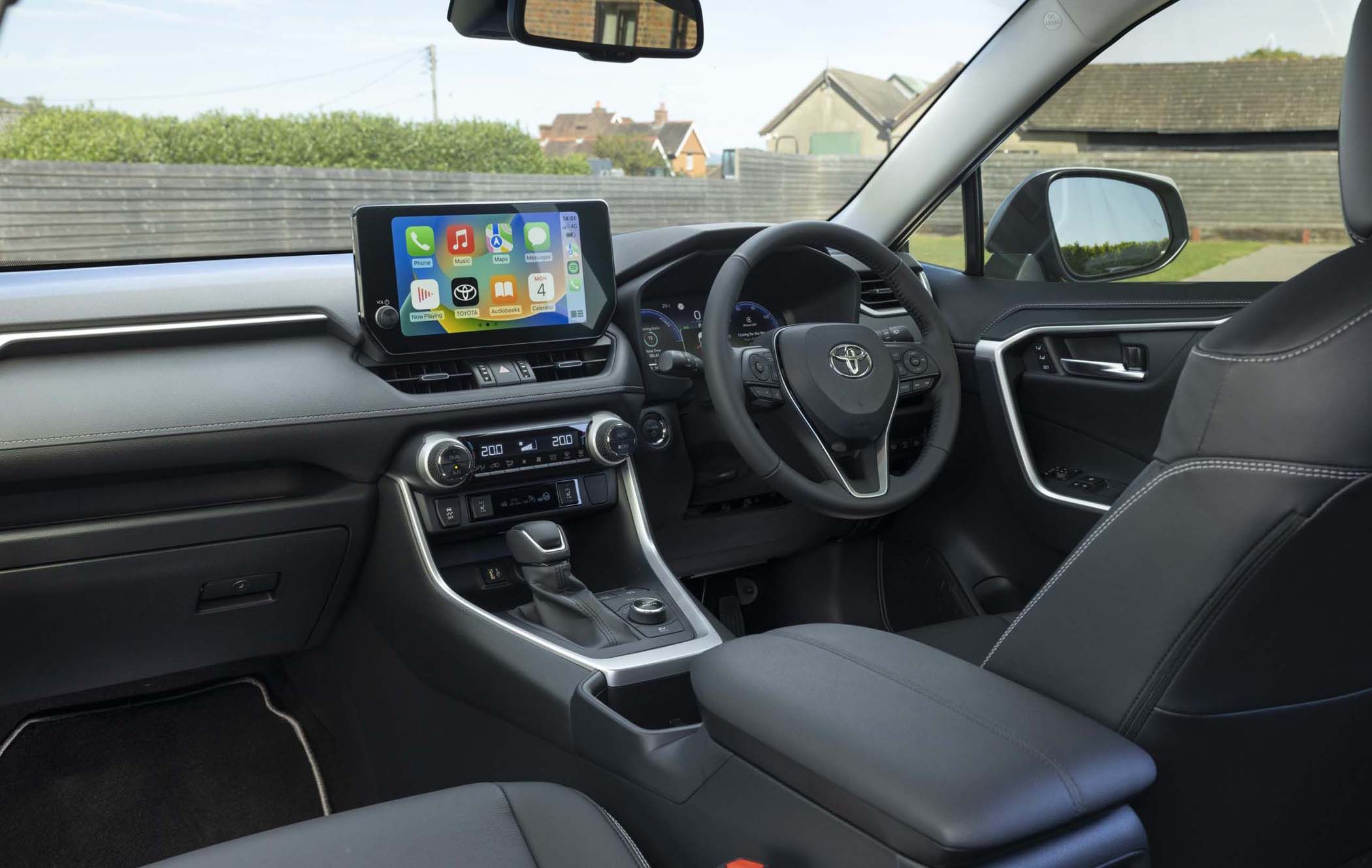 Interior of a Toyota RAV4 Excel featuring a touchscreen display with apps, sleek dashboard, steering wheel, and gear shift. Black leather seats visible.