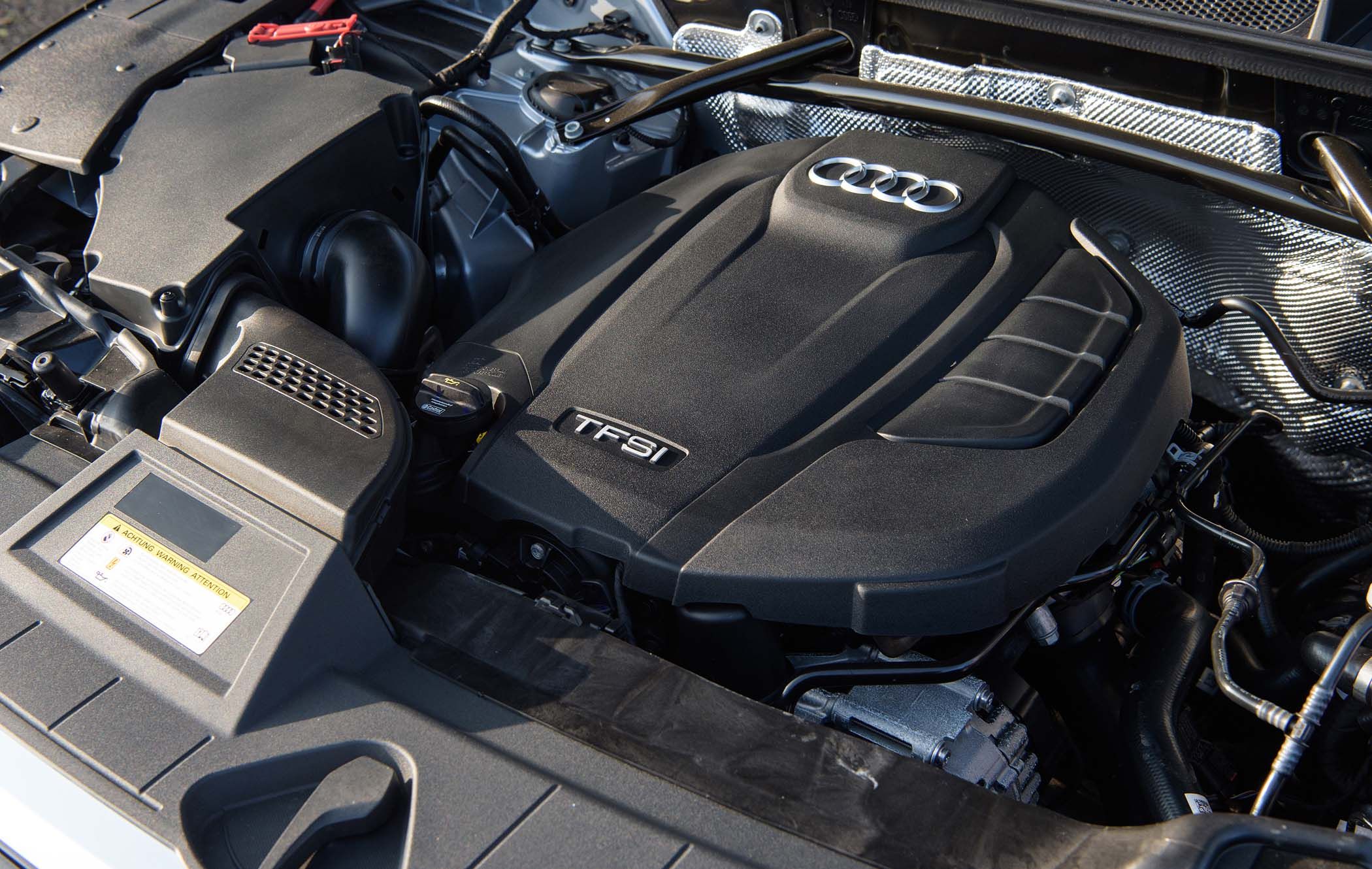 Close-up of an Audi Q5 engine featuring the TFSI label, showcasing various components and a sleek black cover with the Audi logo.