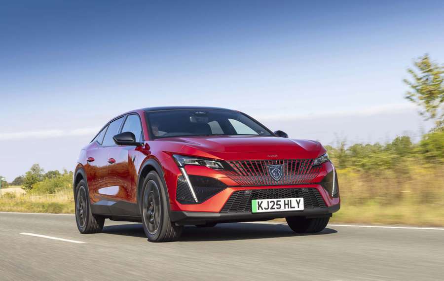 Red Peugeot E-408 driving on a road with a clear blue sky and greenery in the background.