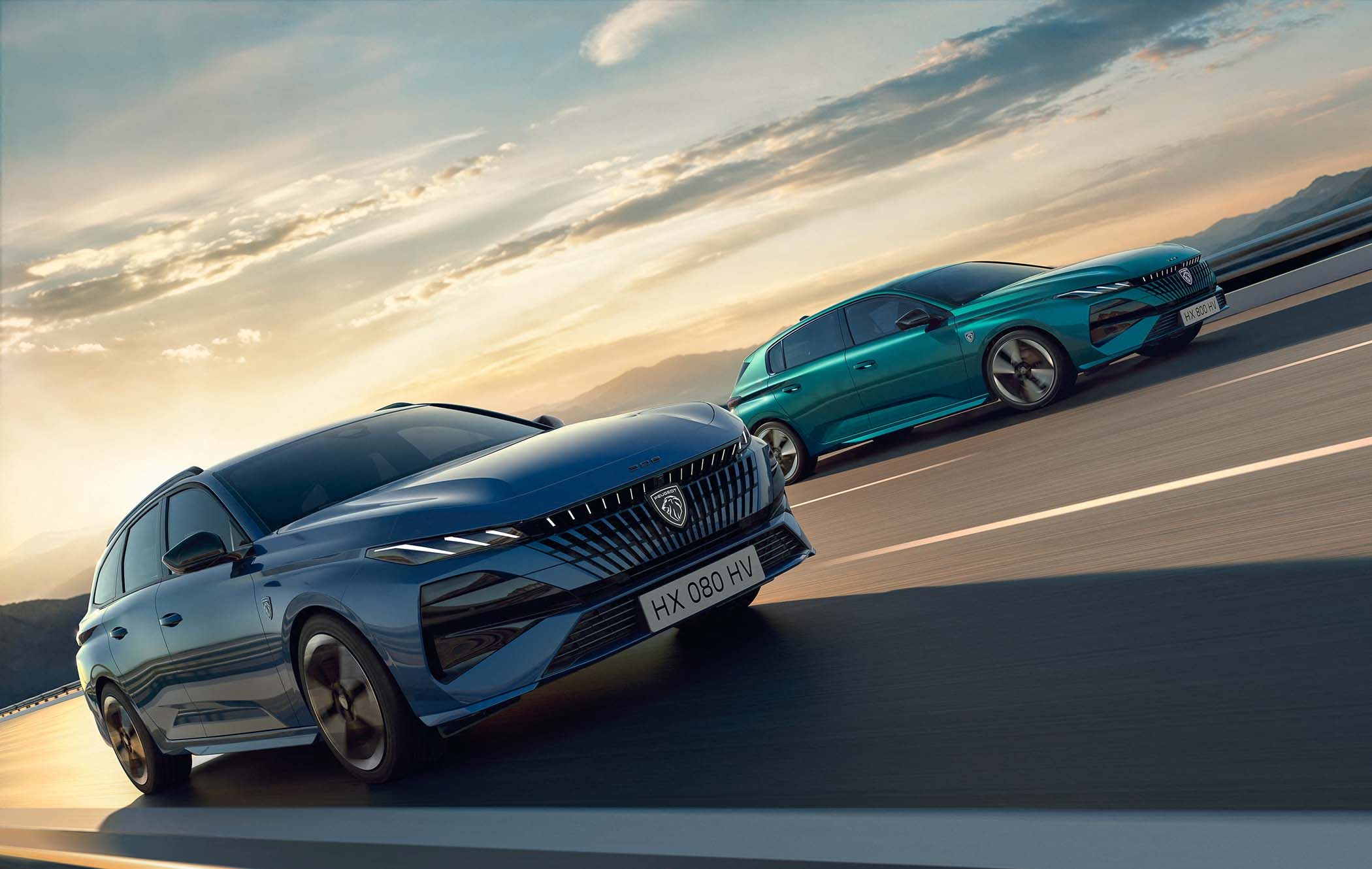 Two Peugeot 308s, one blue and one teal, driving on a highway at sunset with mountains in the background.