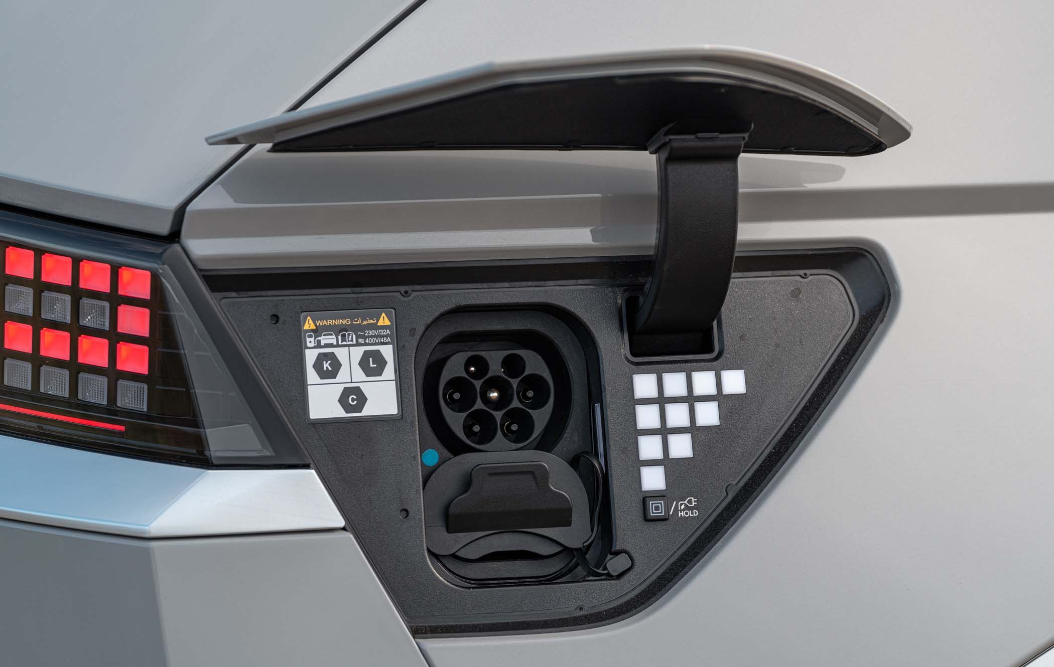 Close-up of a Hyundai IONIQ 5 charging port with the cover open, showing the connector and various icons on a sleek, modern vehicle.
