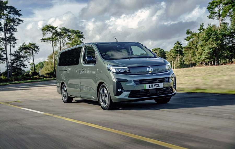 A grey Vauxhall Vivaro Life Electric driving on a road with trees and a cloudy sky in the background.