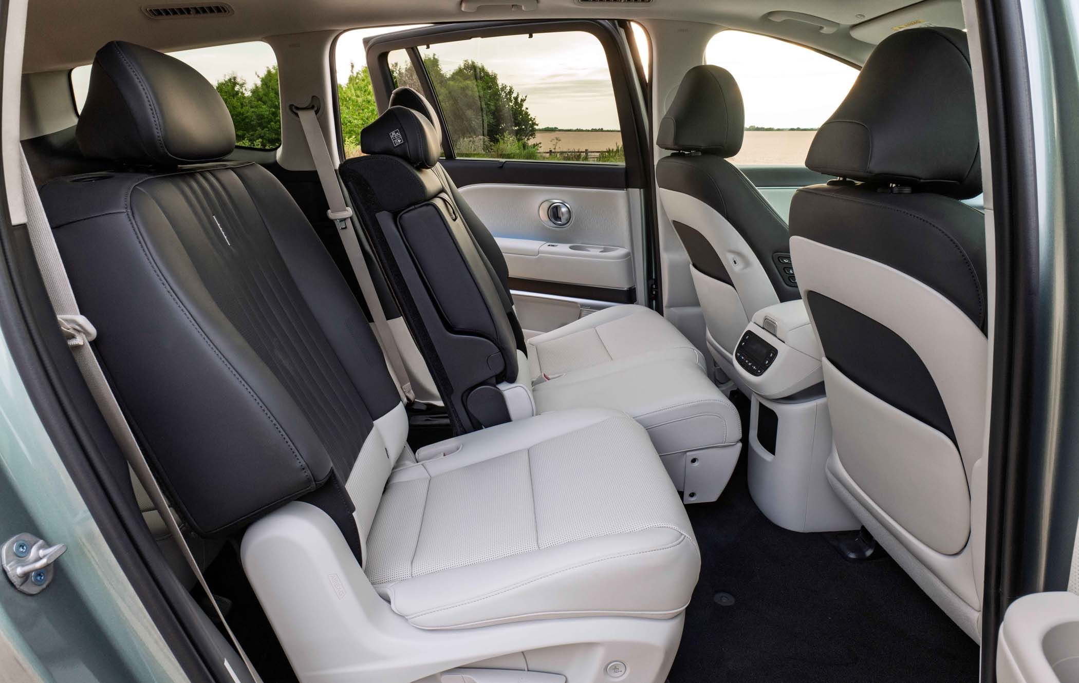Interior of a Hyundai IONIQ 9 showing black and white leather seats, with one seat folded forward, against a backdrop of trees seen through the window.