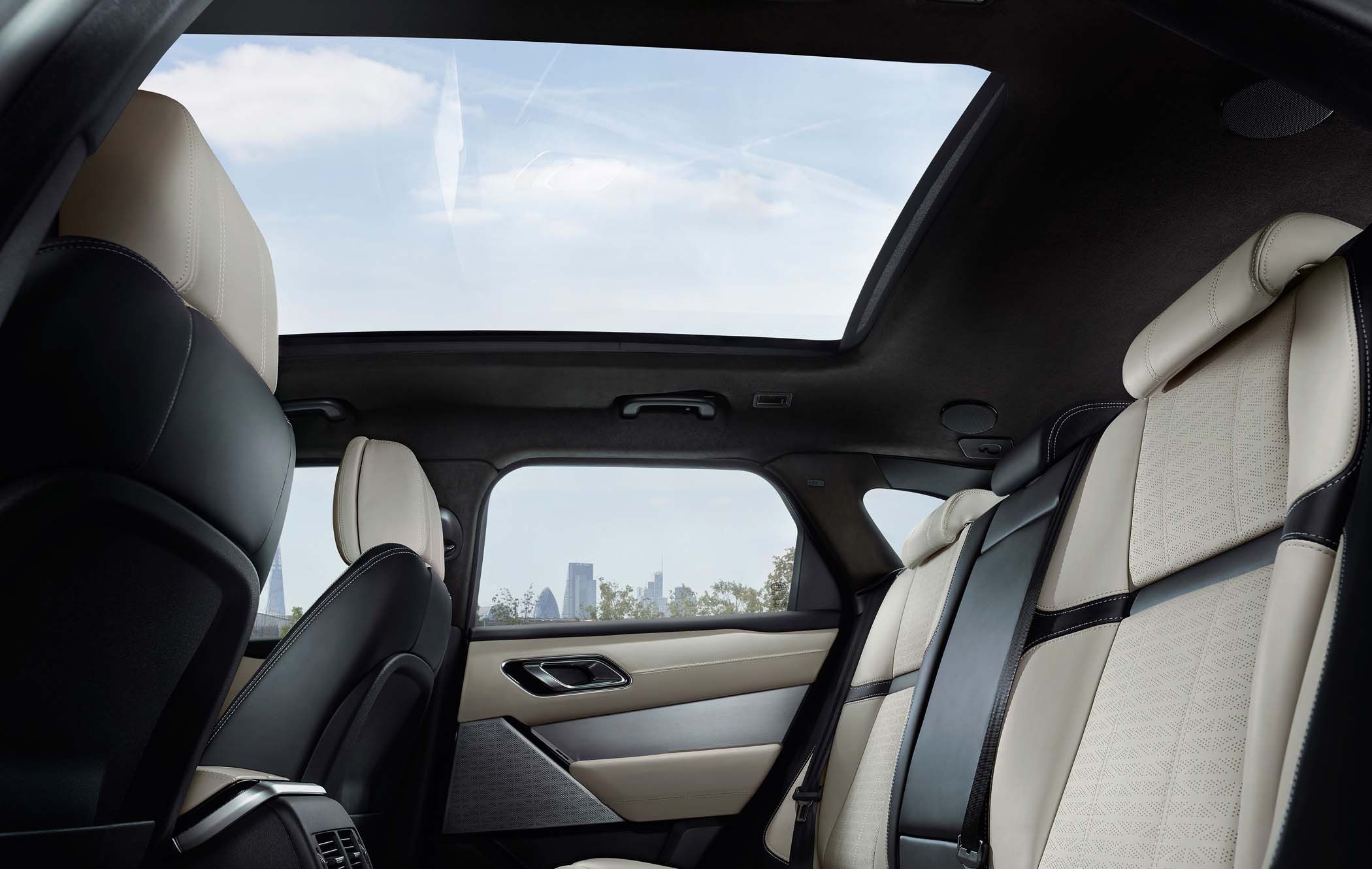 Range Rover Velar interior featuring cream leather seats, a panoramic sunroof, and a view of a city skyline through the side window.