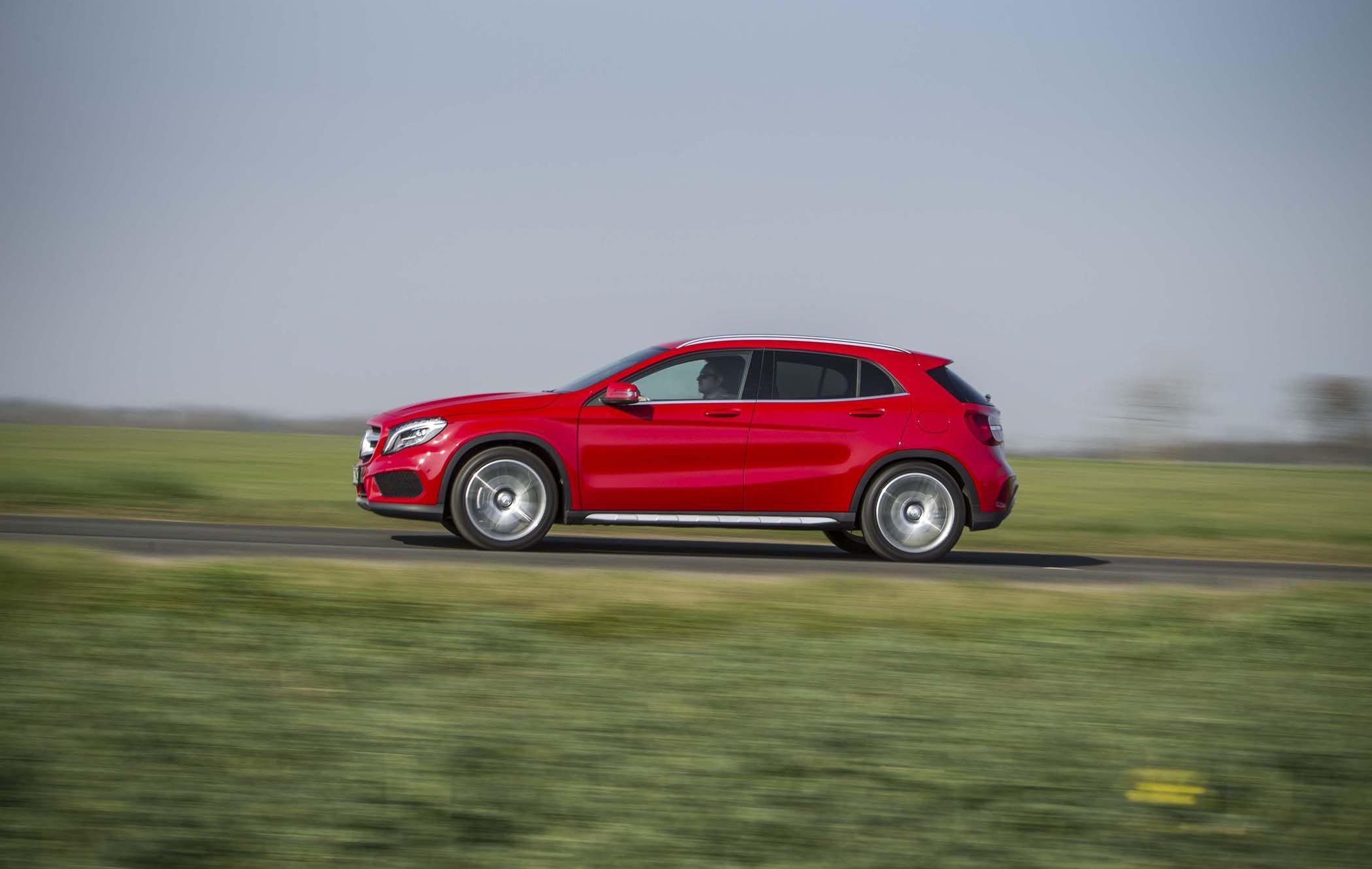 Red Mercedes GLA driving on a rural road with blurred grassy fields in the background, indicating motion.