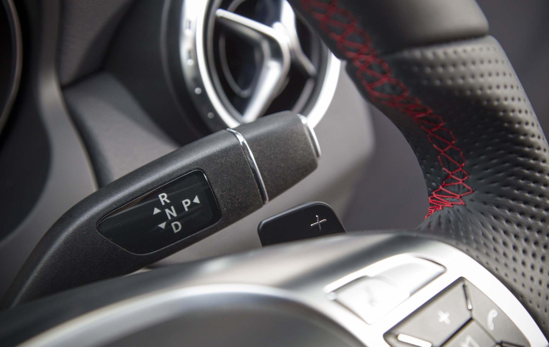 Close-up of a Mercedes GLA's steering wheel with red stitching, showing a gear shifter, and an air vent in the background.